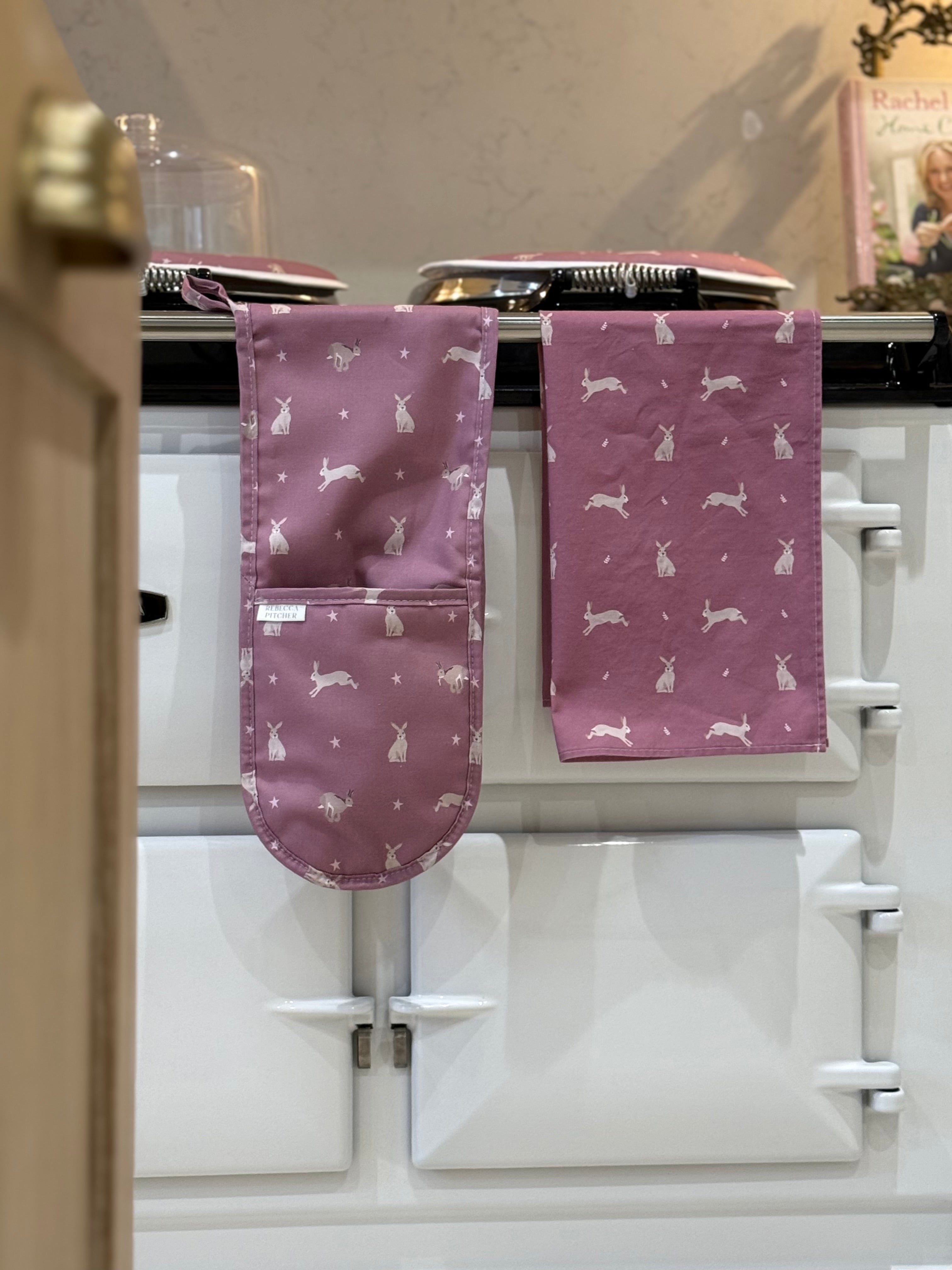 Pink kitchen towel and oven gloves with hare patterns hanging on a stove.