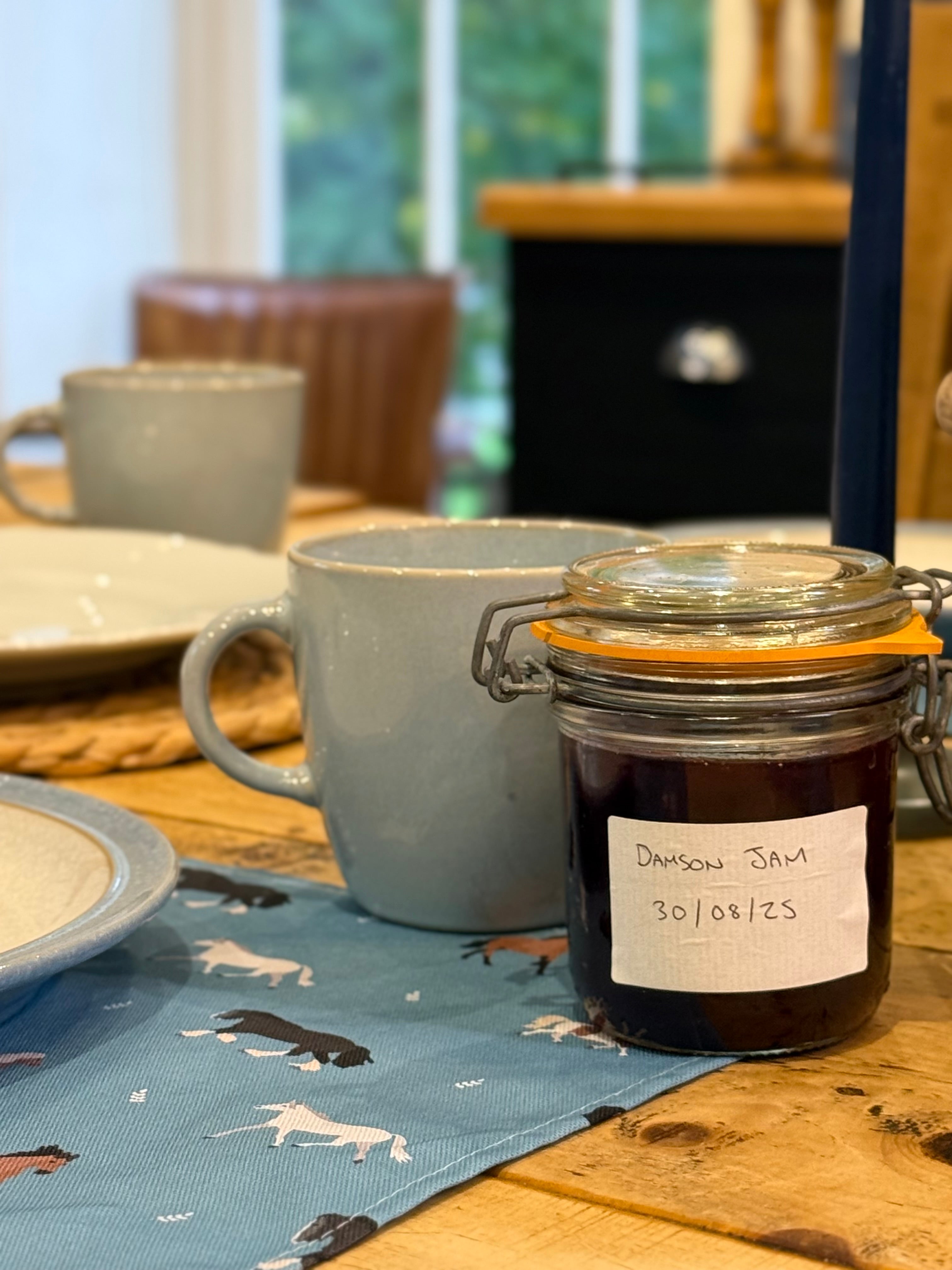 Jar of damson jam on a table with mugs and a horse print placemat