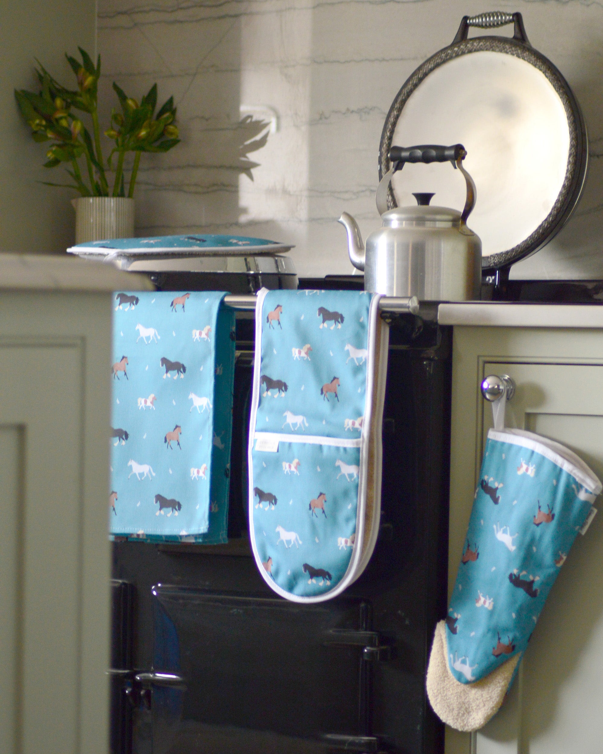 Kitchen scene with a black range cooker featuring blue oven mitts and hob covers with horse pattern.