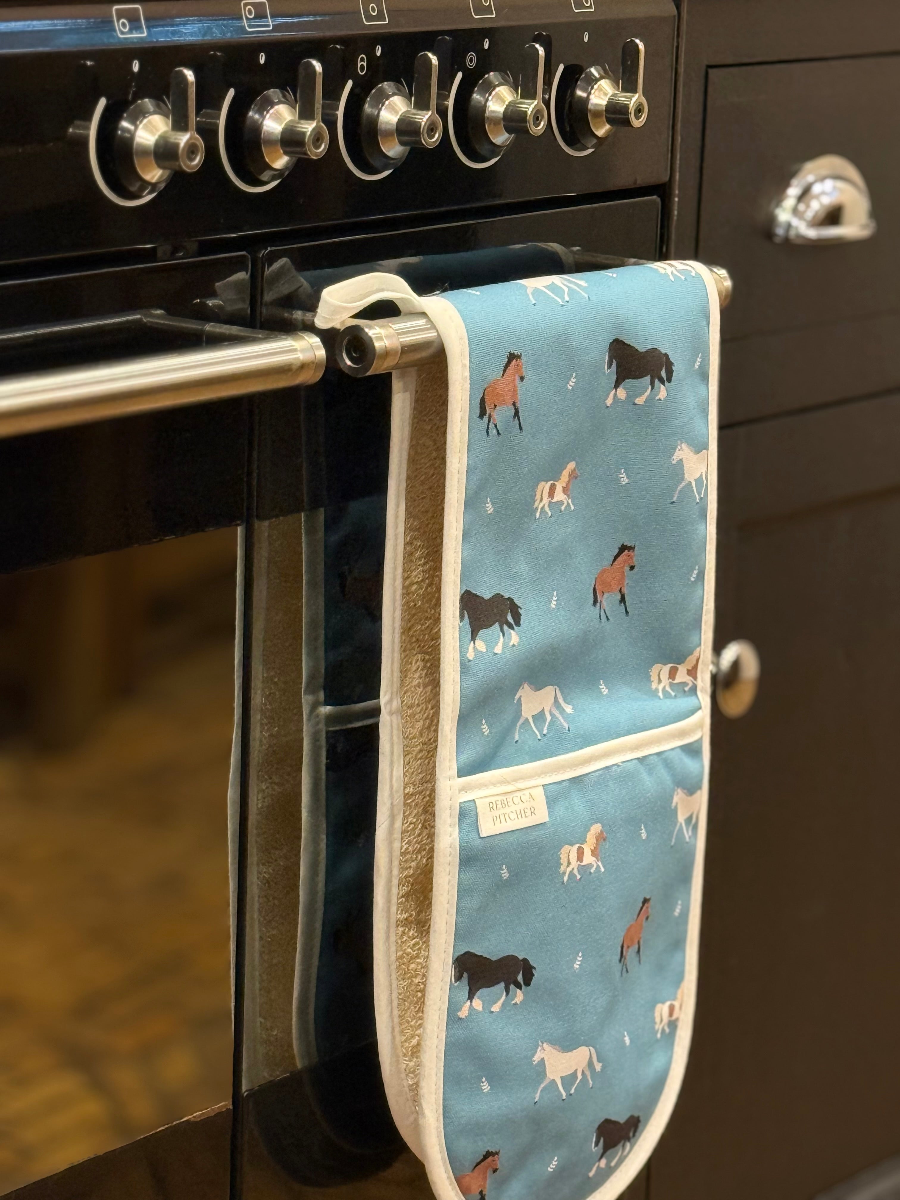 horse fabric double ovengloves hanging on a cooker rail