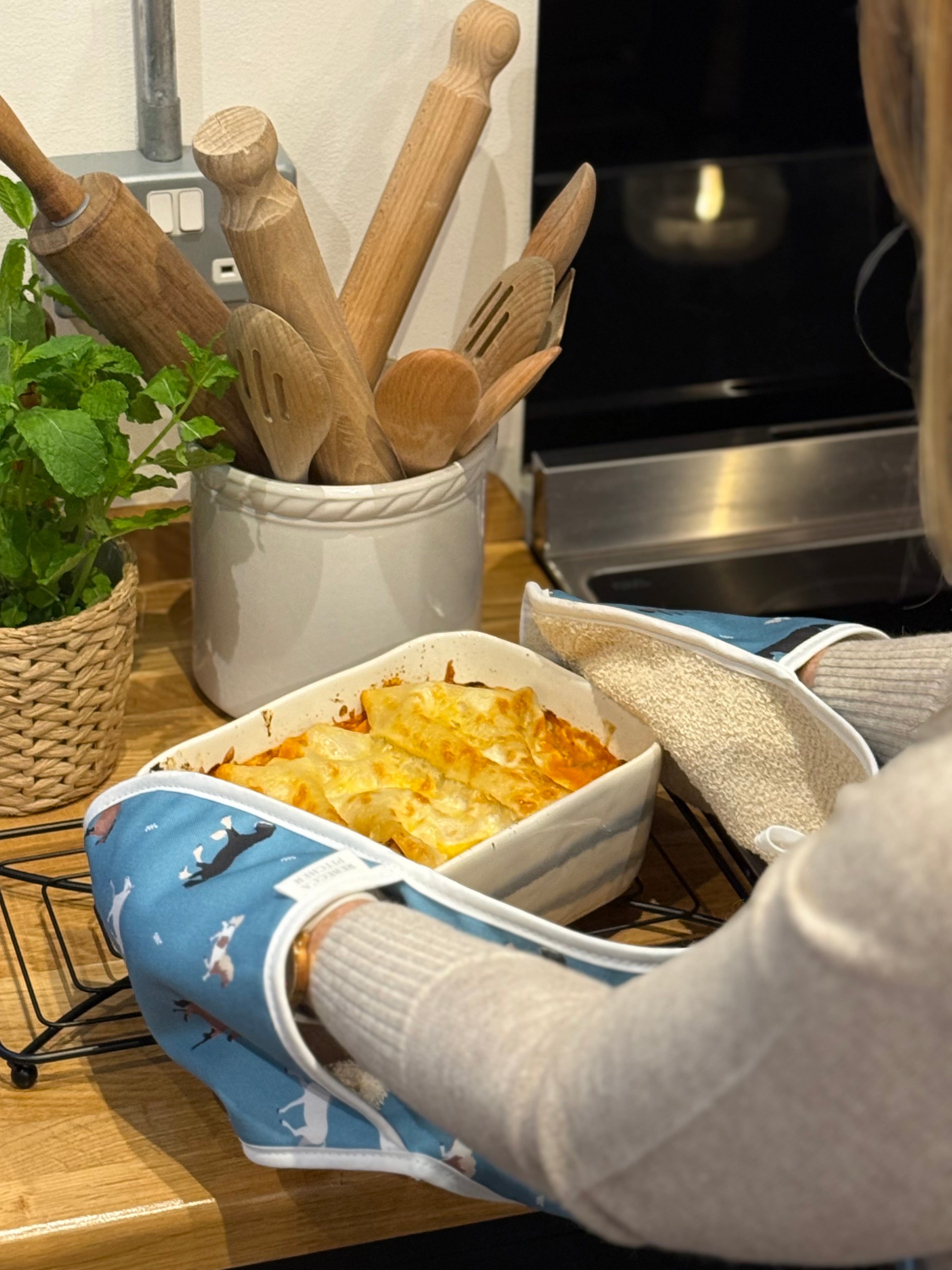 Person using blue horse patterned double oven gloves to put a lasagne on the kitchen worktop