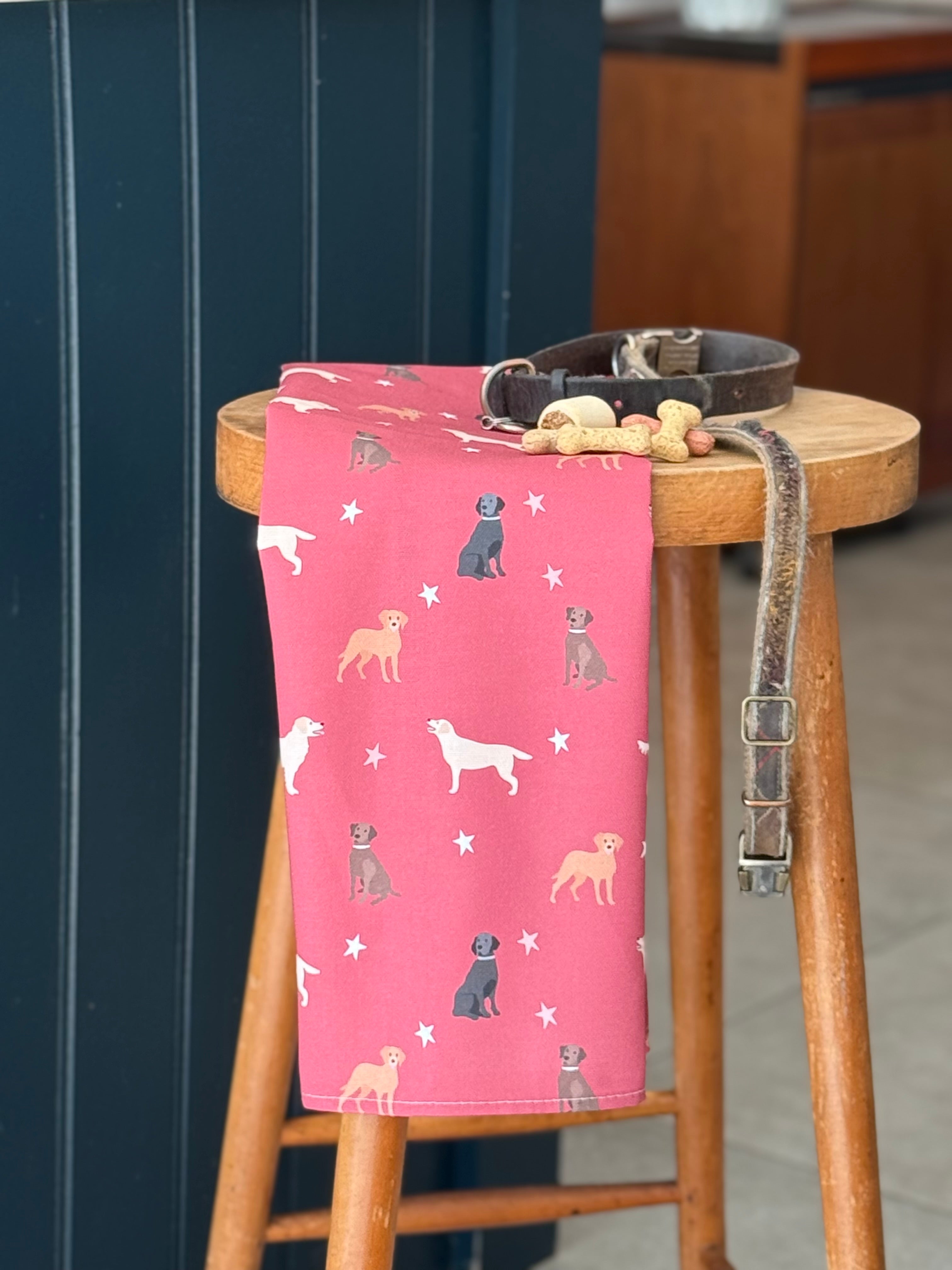Red Labrador Tea Towel with dog illustrations on a wooden stool against a blue kitchen island.
