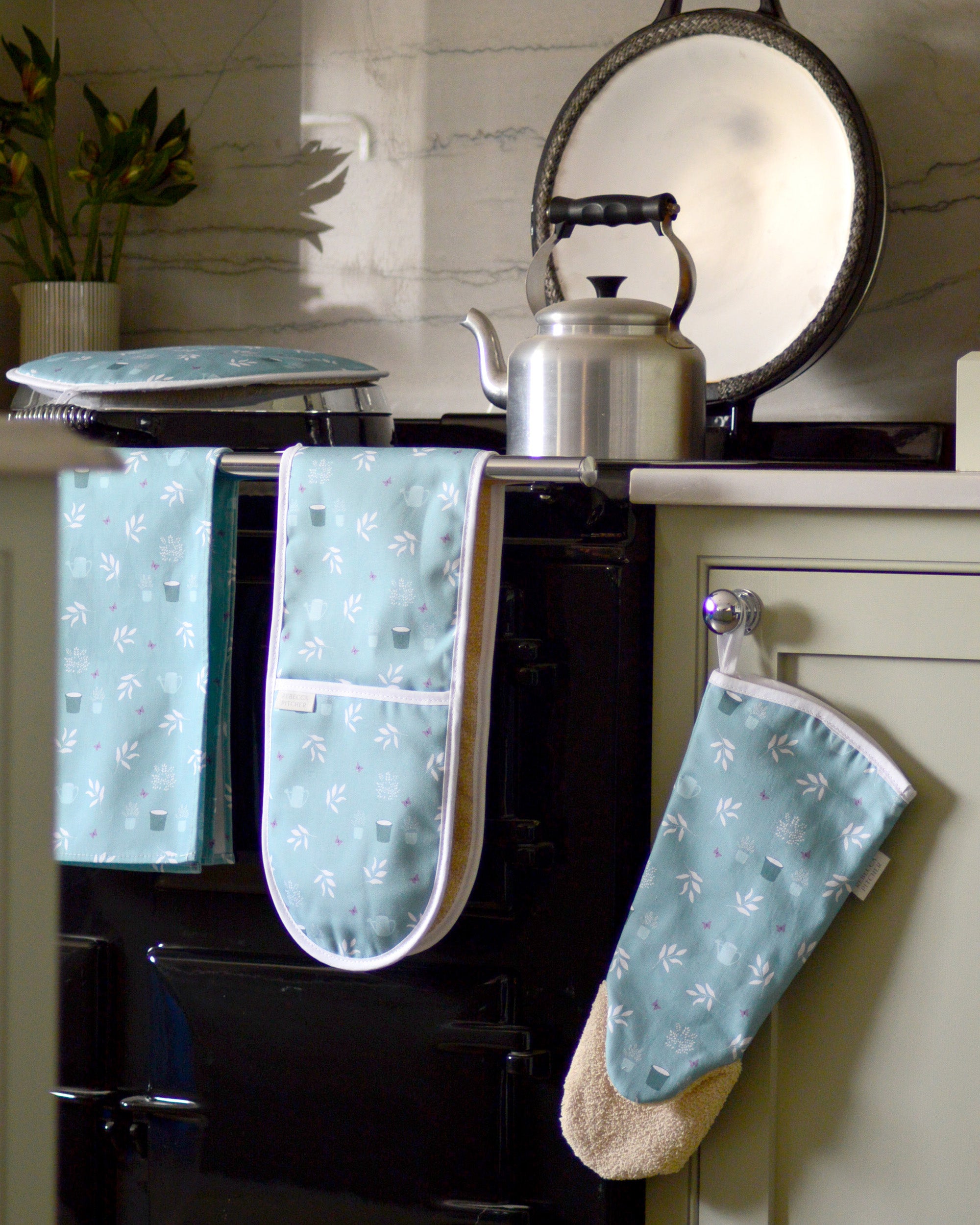 Teal garden design oven mitts and gauntlet hanging on a black stove in a kitchen.