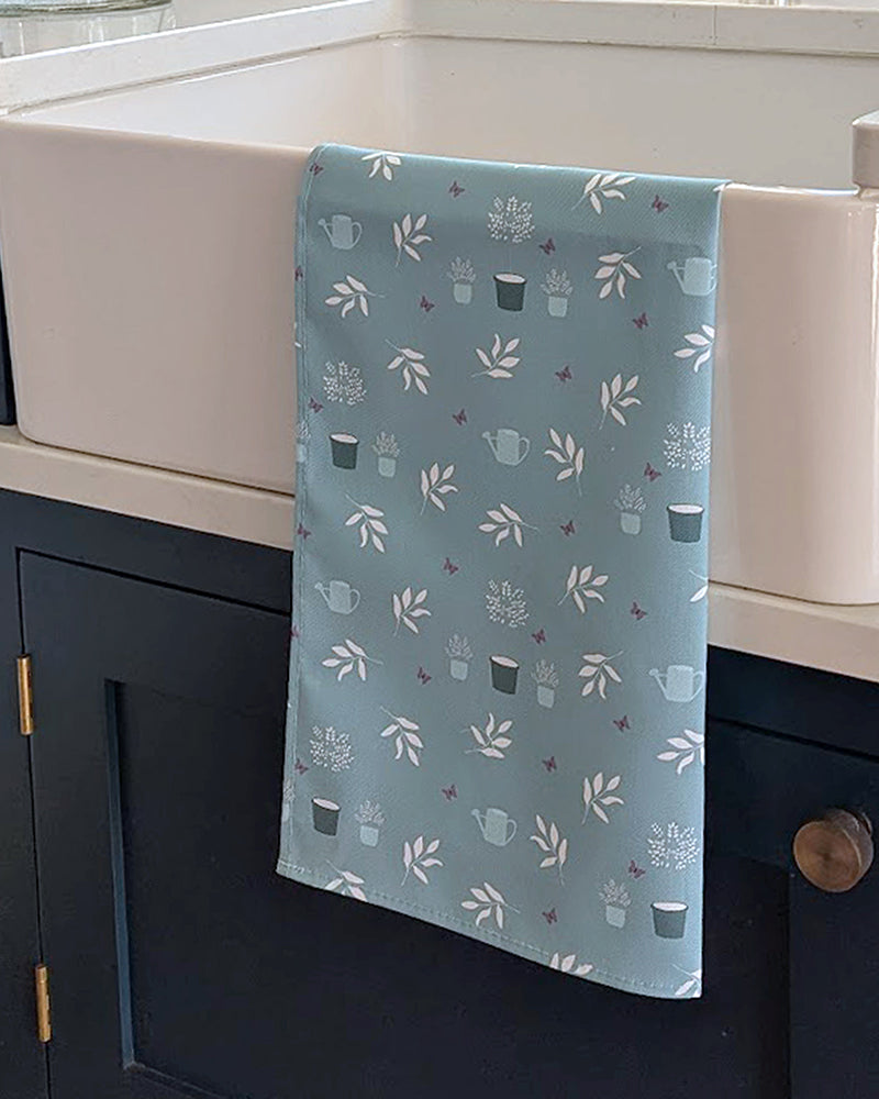 Duckegg blue tea towel with cottage garden pattern hanging on a kitchen sink.