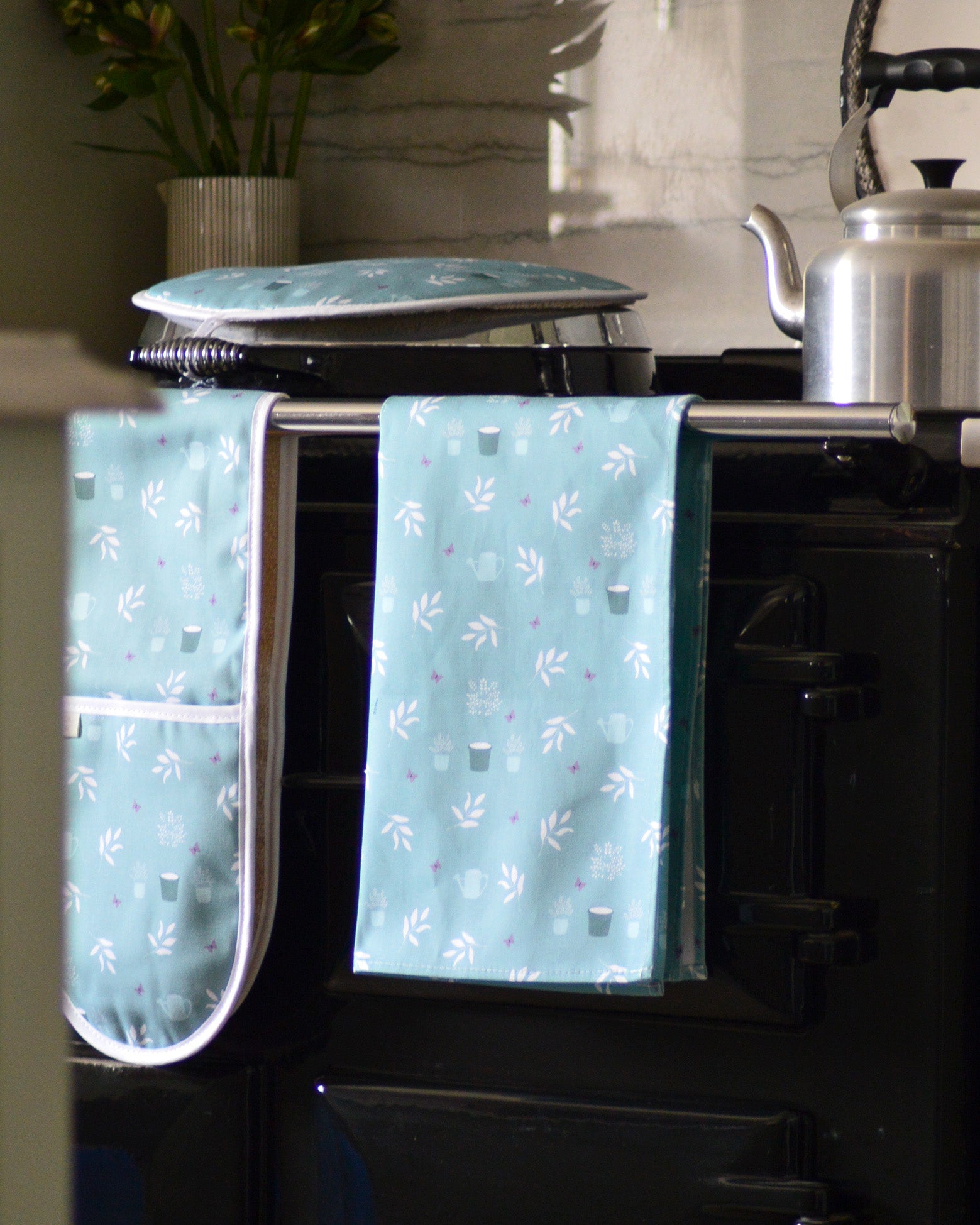 Teal floral patterned kitchen towel hanging on a stove handle.