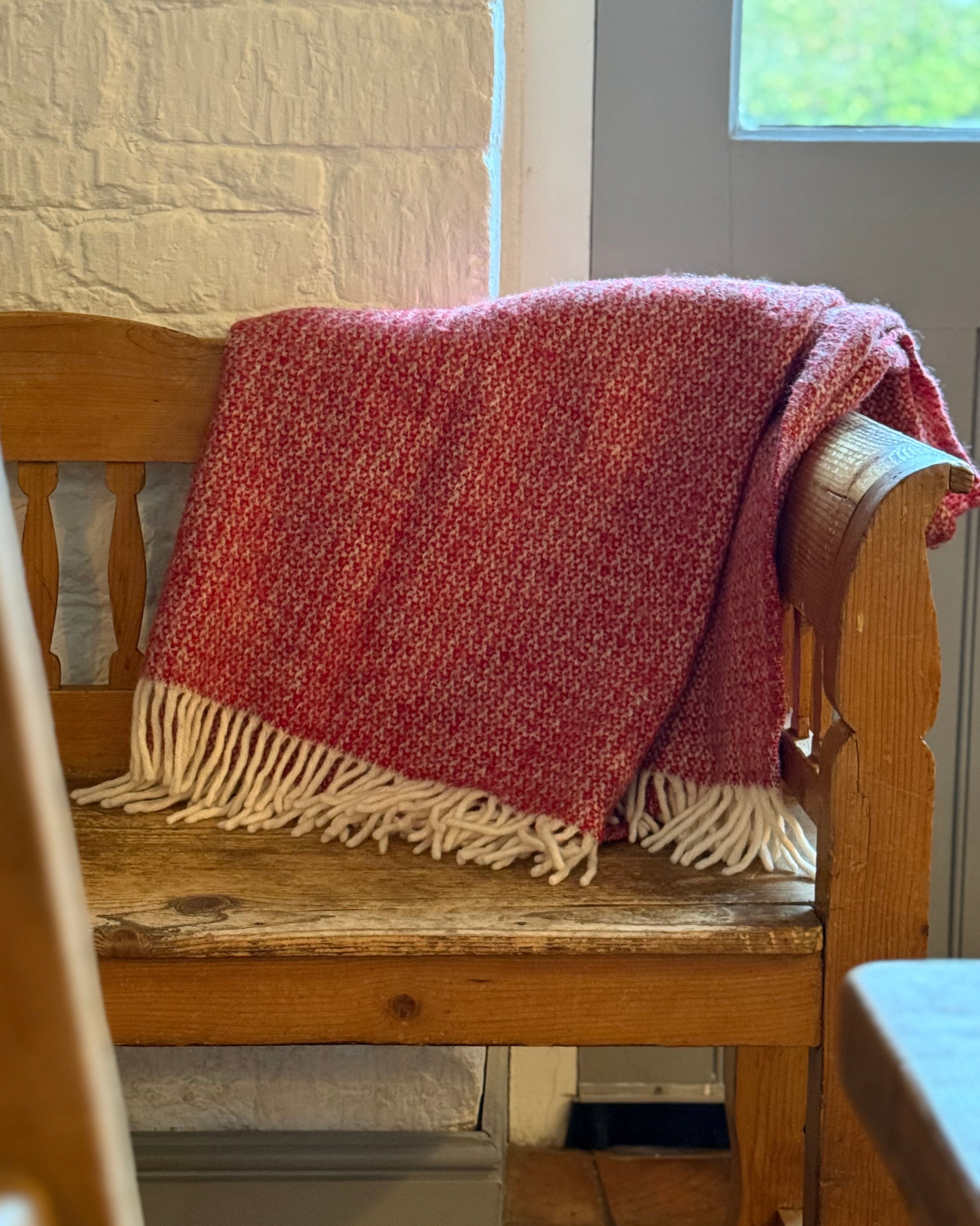 Red blanket with fringes draped over a wooden bench indoors.