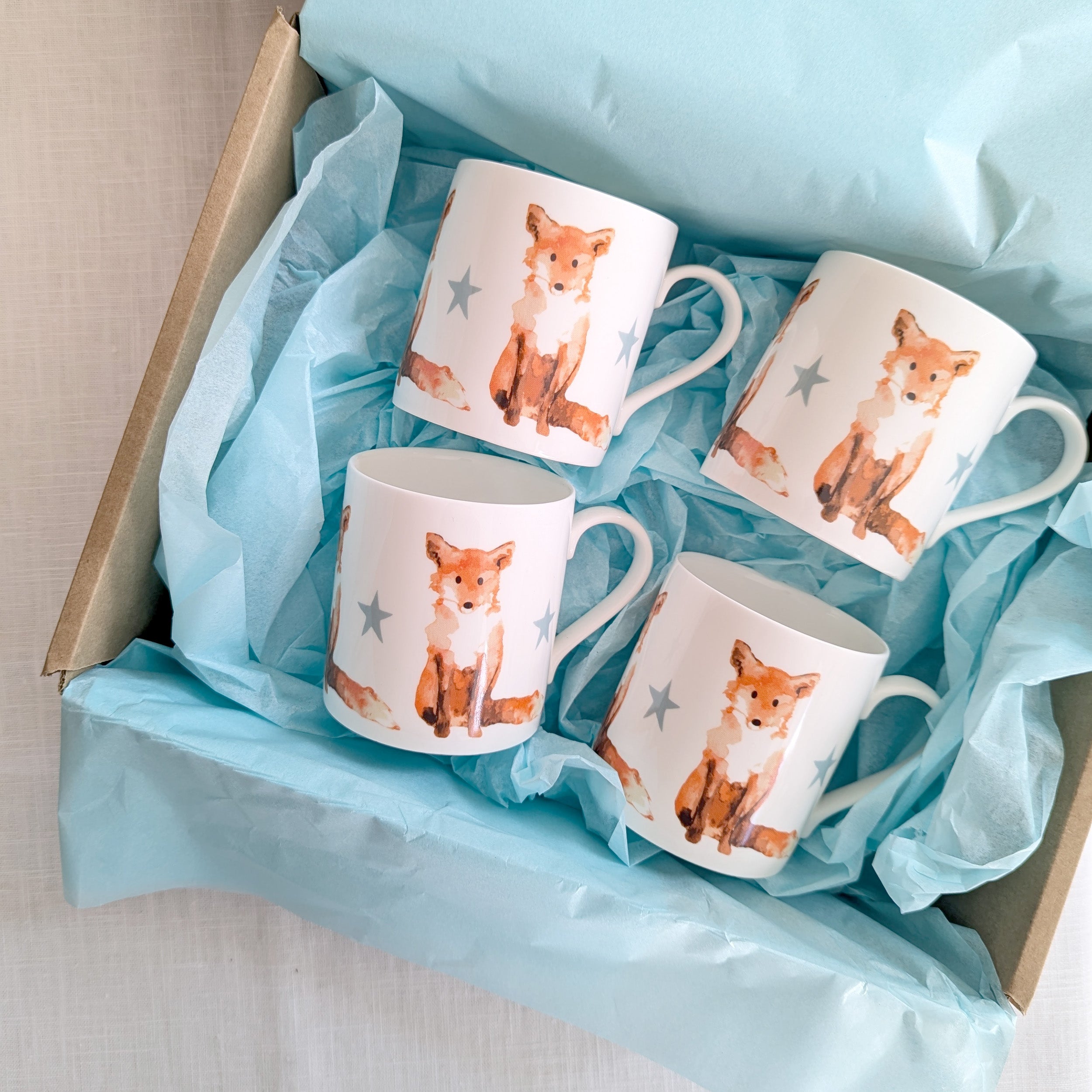 Four mugs with fox illustrations in a box lined with blue tissue paper