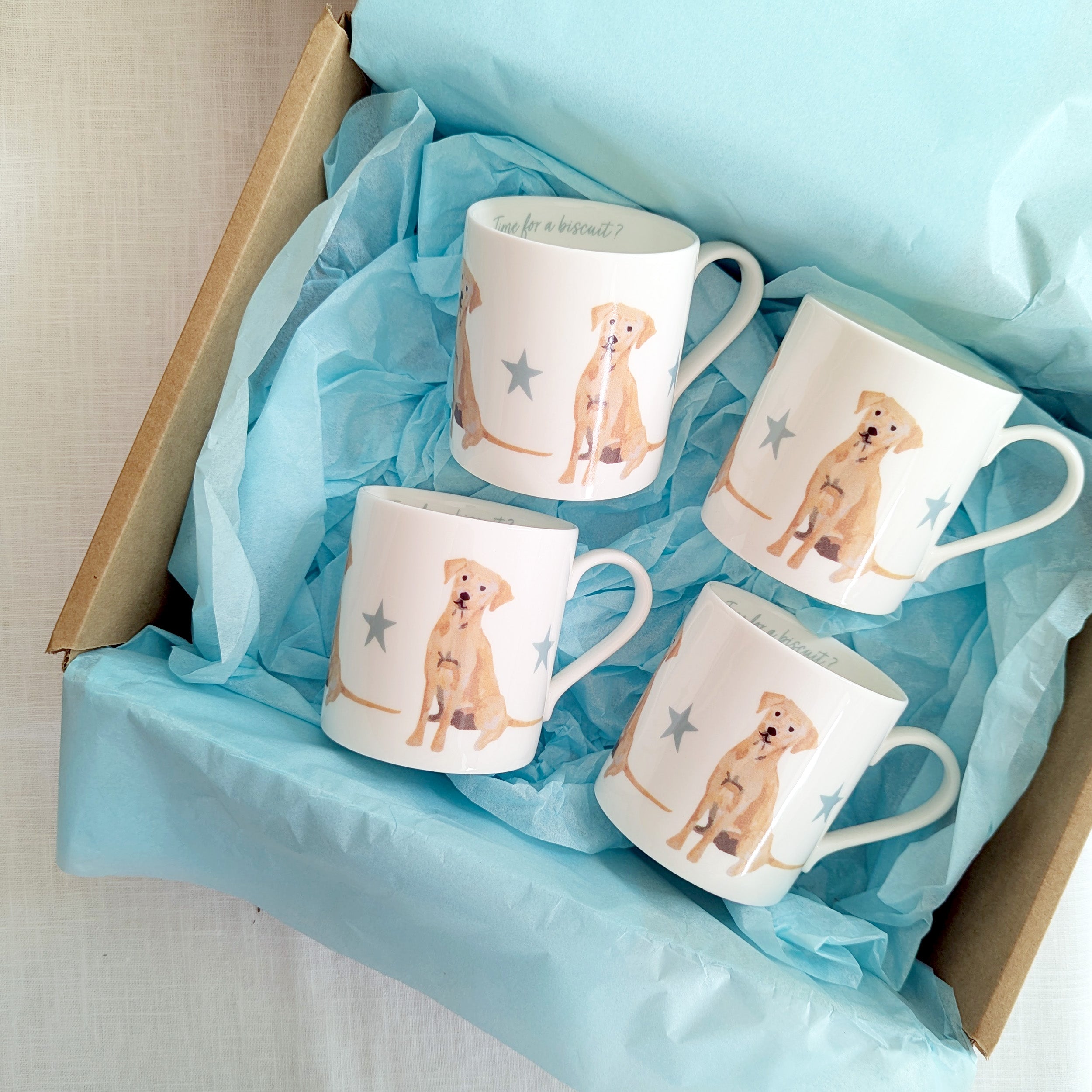 Four mugs with golden labrador dog illustrations in a box lined with blue tissue paper