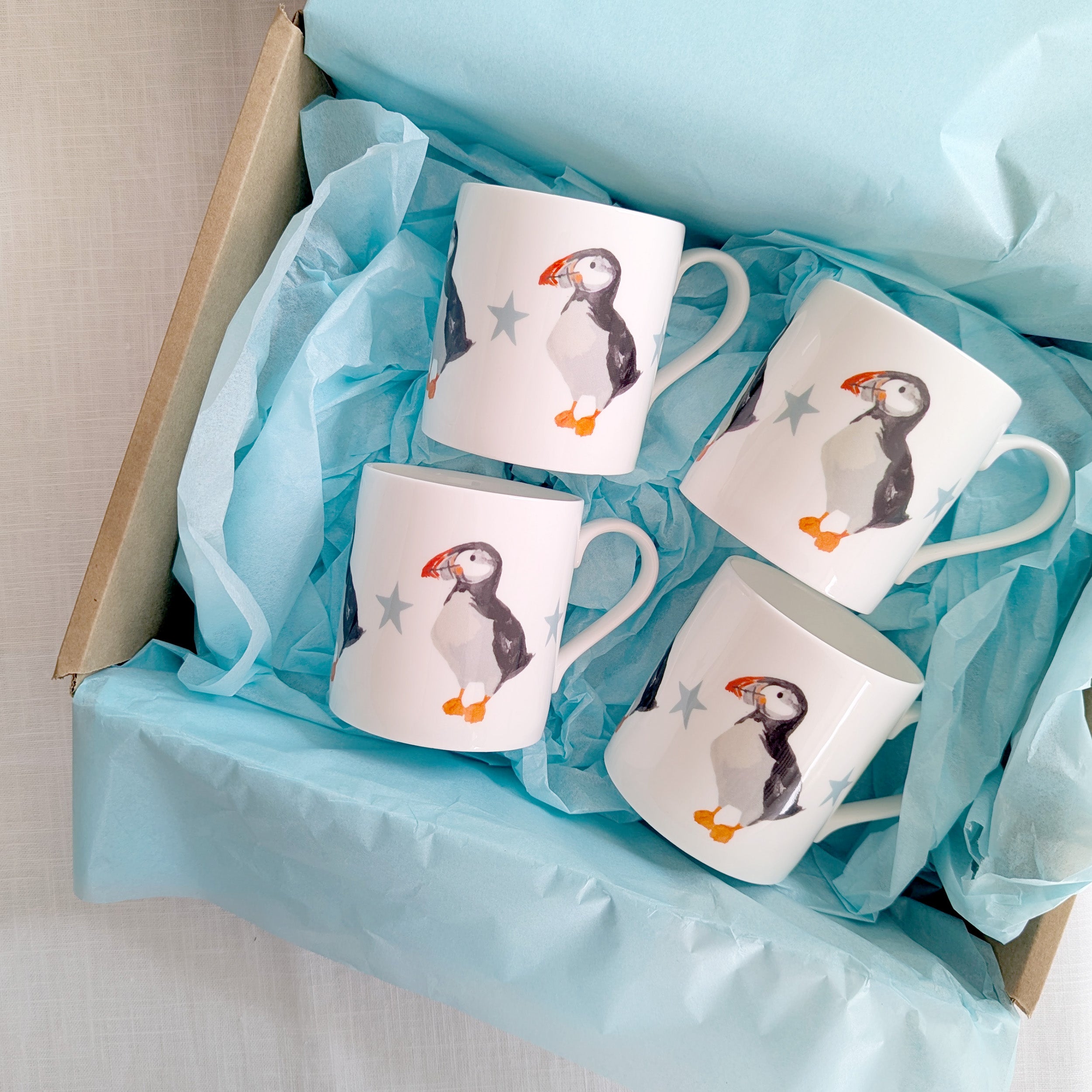 Four ceramic mugs with puffin design in a box with blue tissue paper