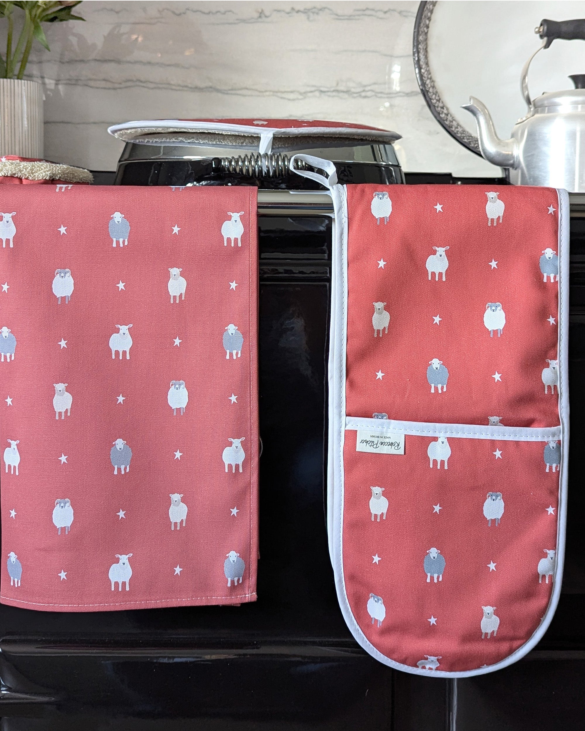 Red oven mitt and tea towel with sheep pattern on a kitchen stove