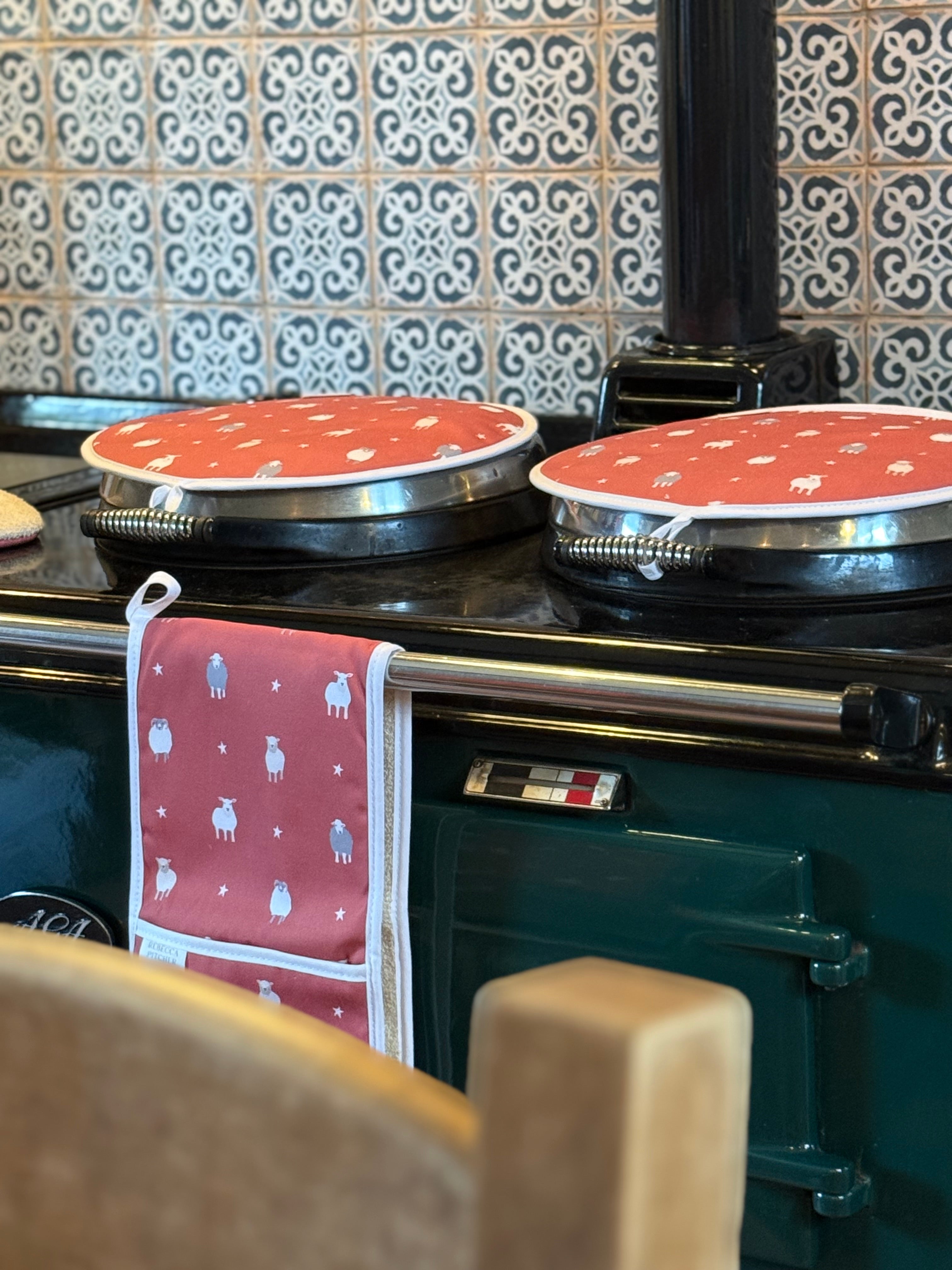 Green Aga range cooker with red sheep design hob covers on a tiled wall background