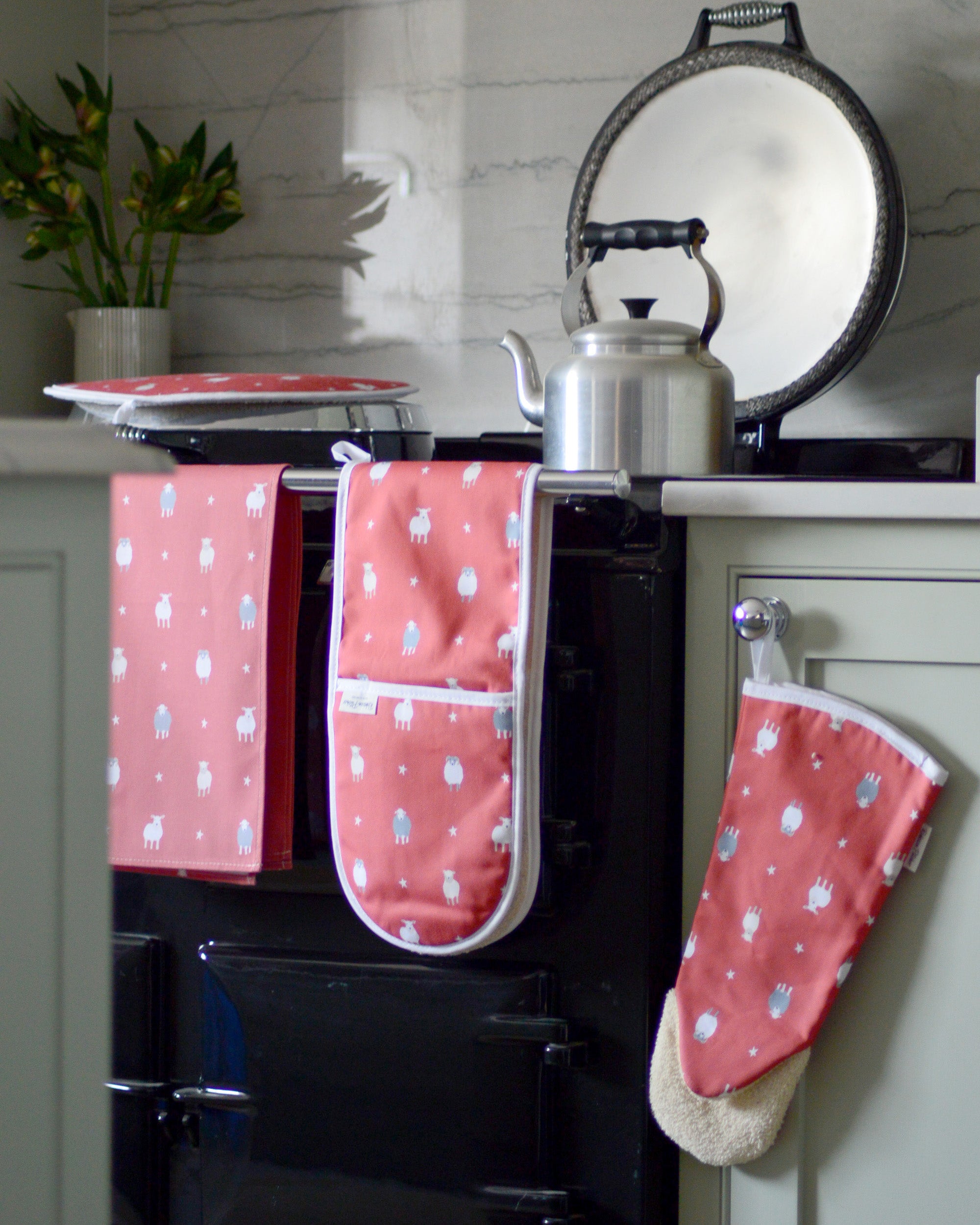 Red sheep patterned oven mitts and tea towel hanging on a black stove.