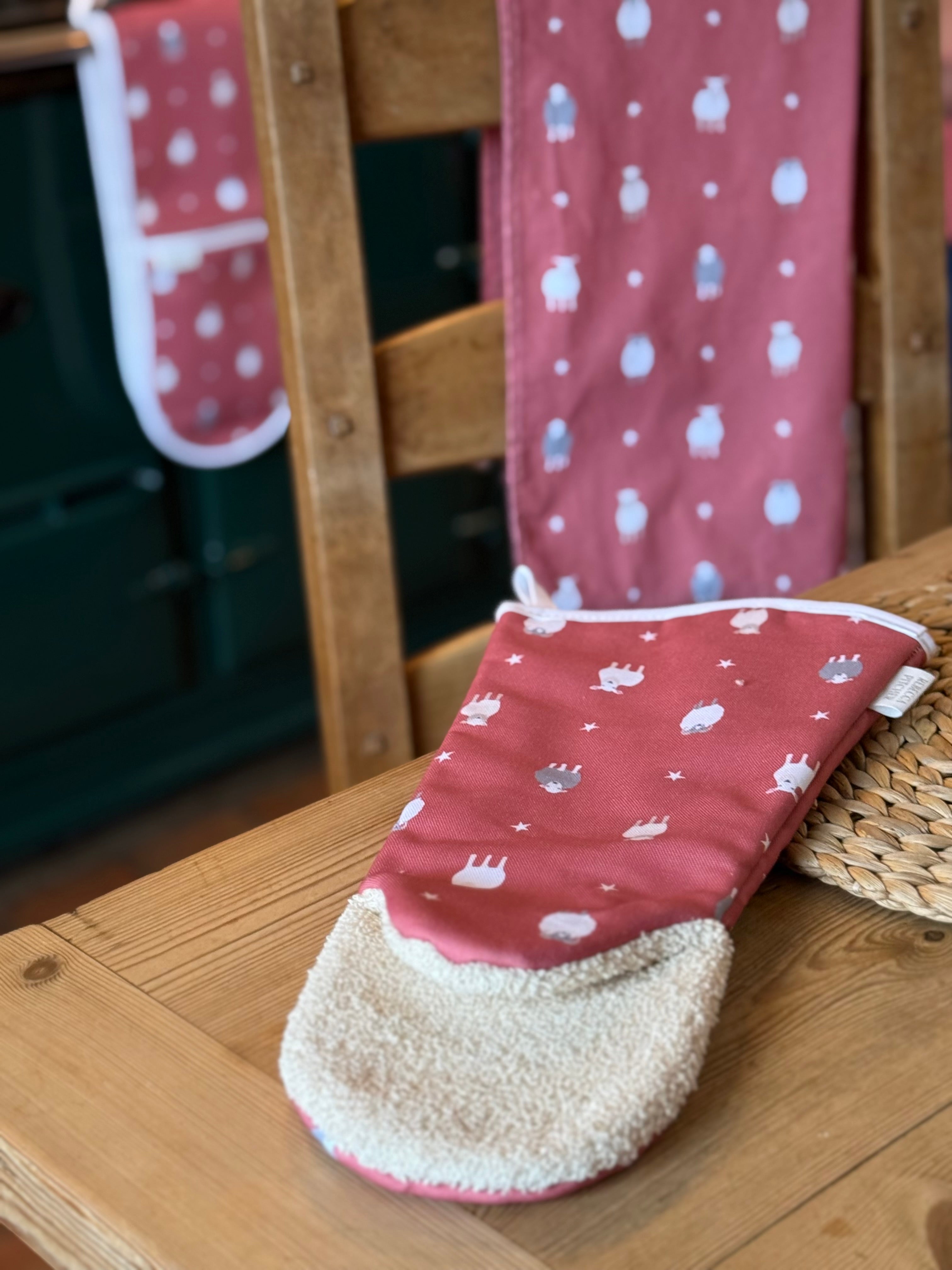 Red oven gauntlet with white sheep patterns on a wooden table