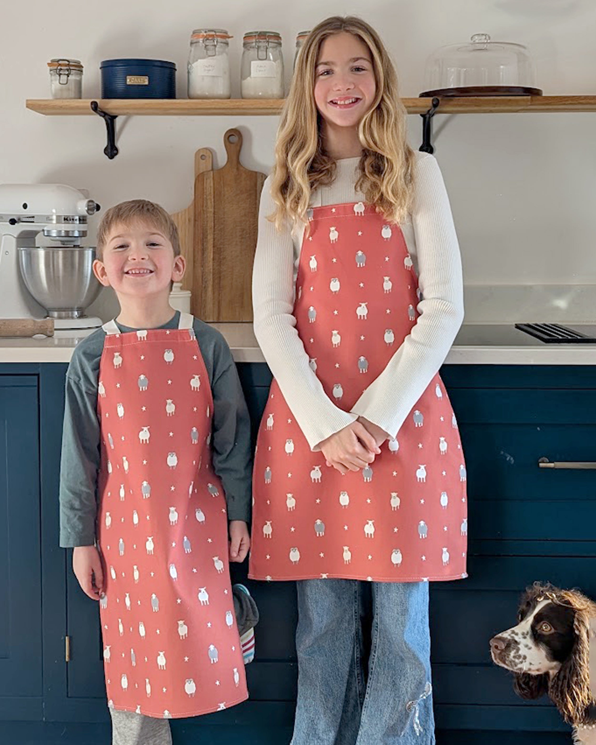 Children wearing red aprons with sheep pattern in a kitchen setting