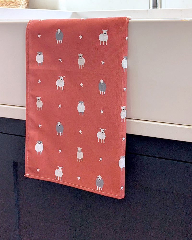 Red tea towel with sheep pattern draped over a kitchen sink
