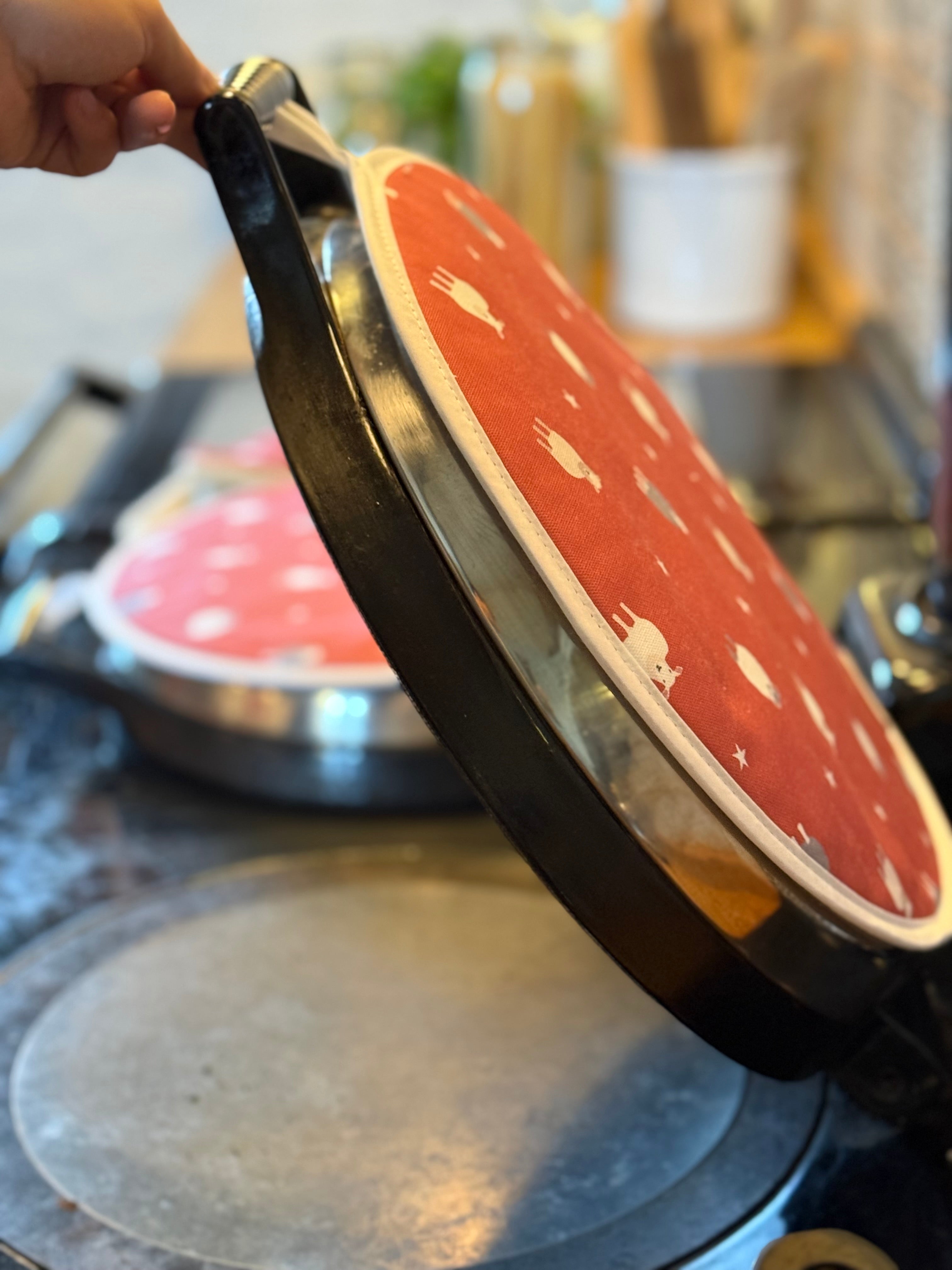 Person lifting a red aga lid with red hob cover with white sheep pattern