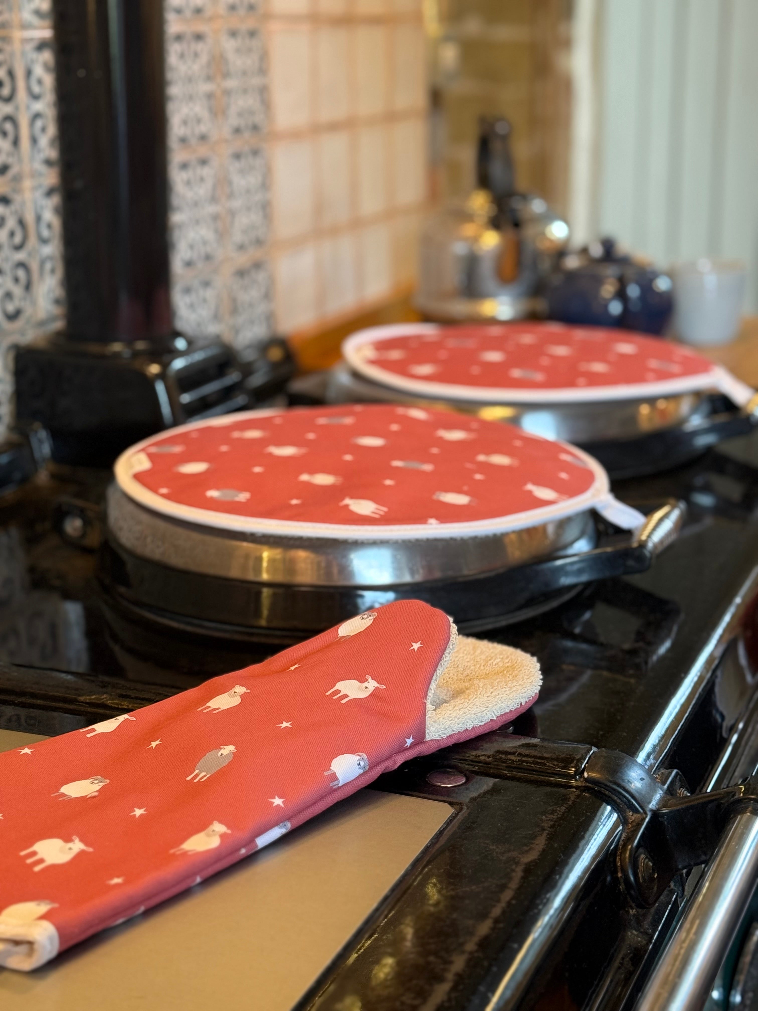 Red oven gauntlet and hob covers with white sheep patterns on a stove