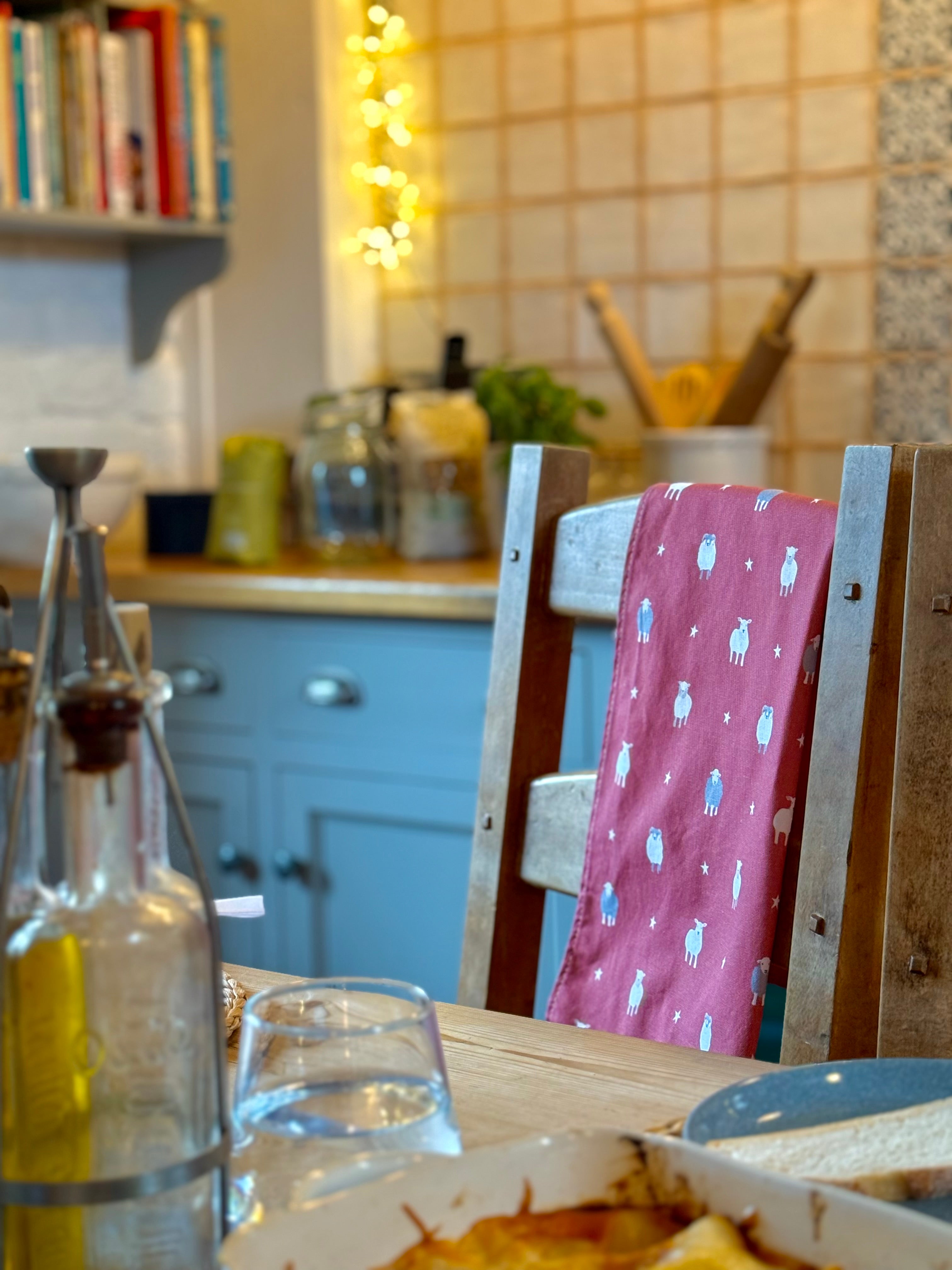 Kitchen scene with a red sheep design tea towel hanging over a wooden chair, table, and kitchen items
