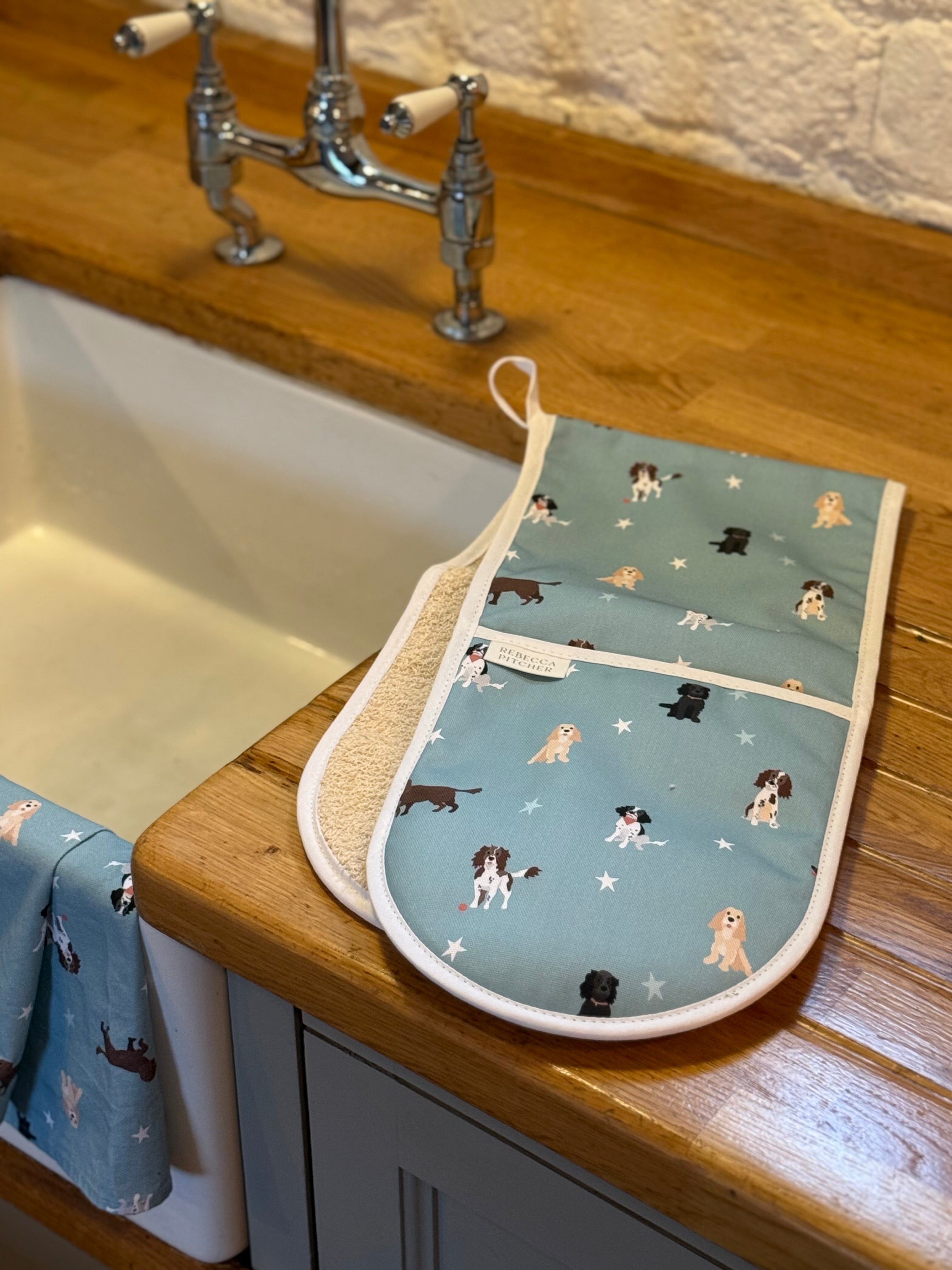 Oven mitt and tea towel with spaniel dog pattern on a wooden kitchen counter.
