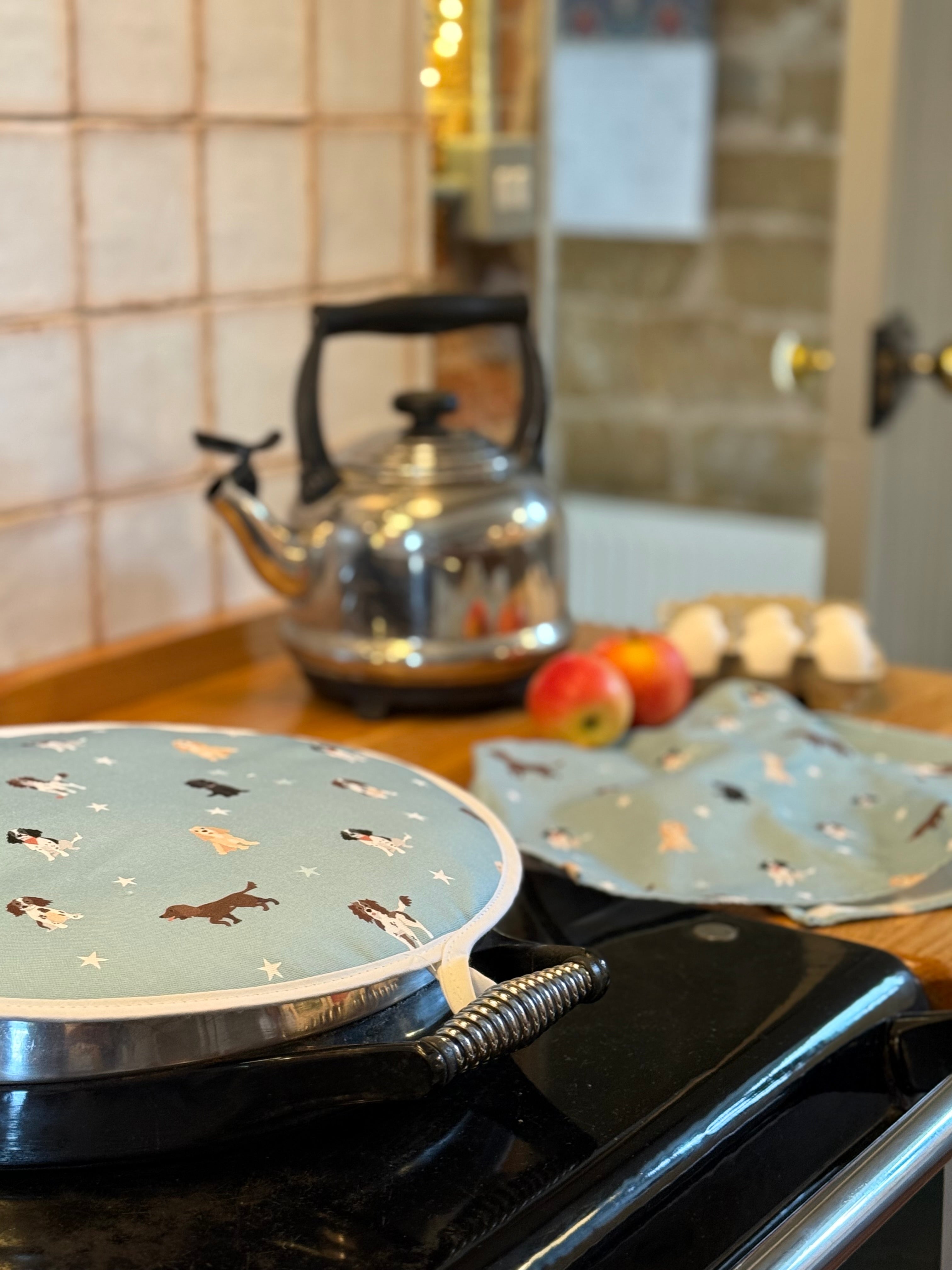 Hob cover with spaniel dog pattern on a stove, with a kettle and apples in the background.
