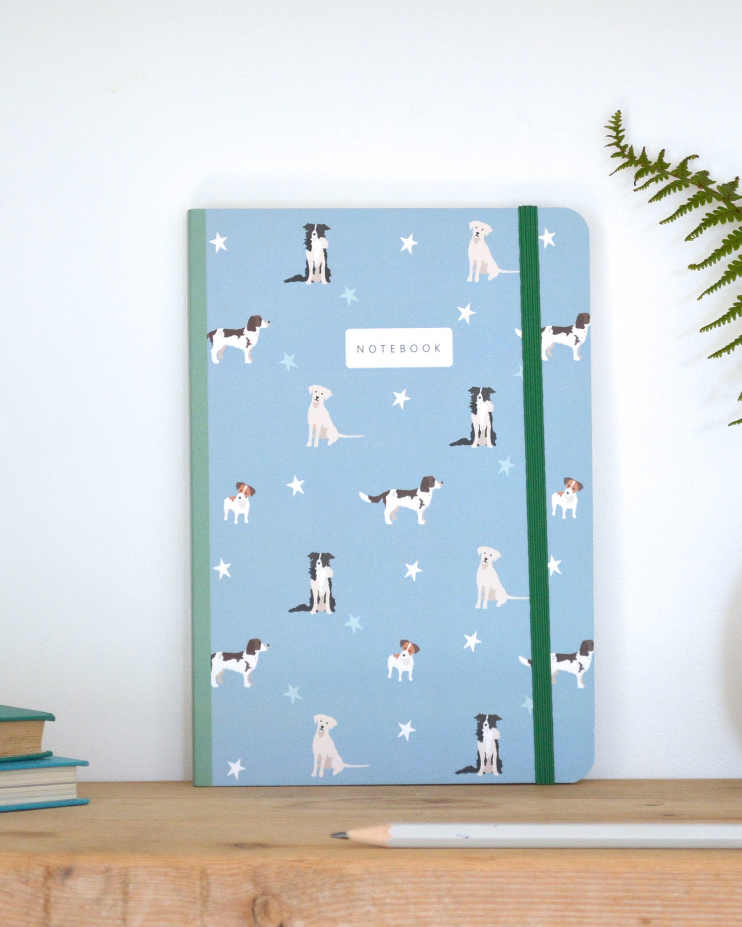 Notebook with dog pattern on a blue background, placed on a wooden surface with a plant in the corner.