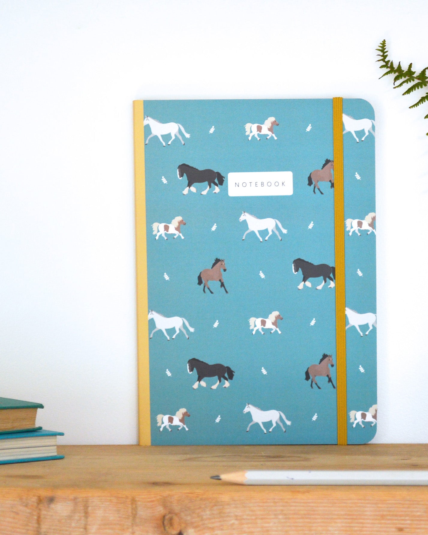 Notebook with horse pattern on a blue background, placed on a wooden surface.