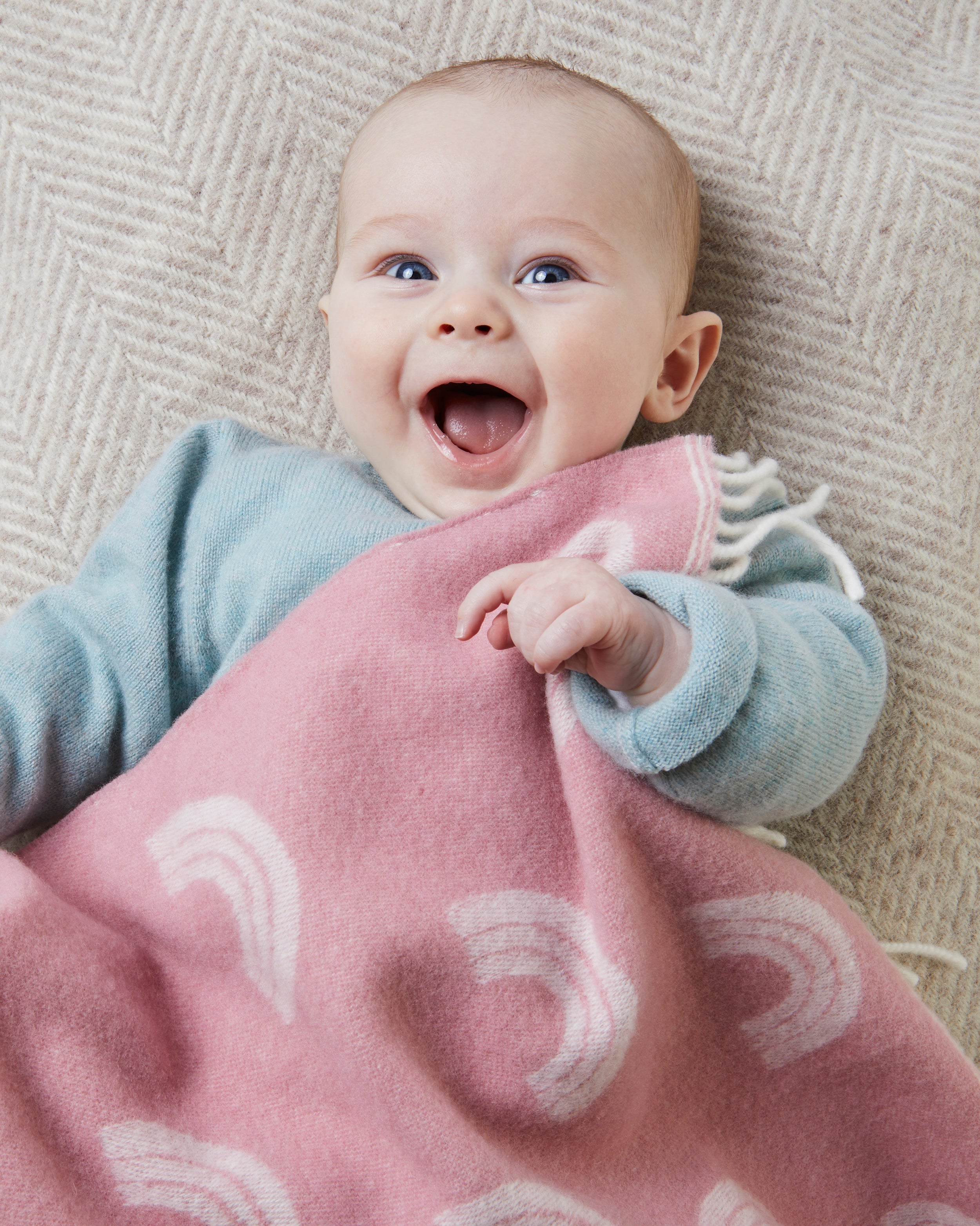 Laughing baby covered in pink rainbow merino wool baby blanket