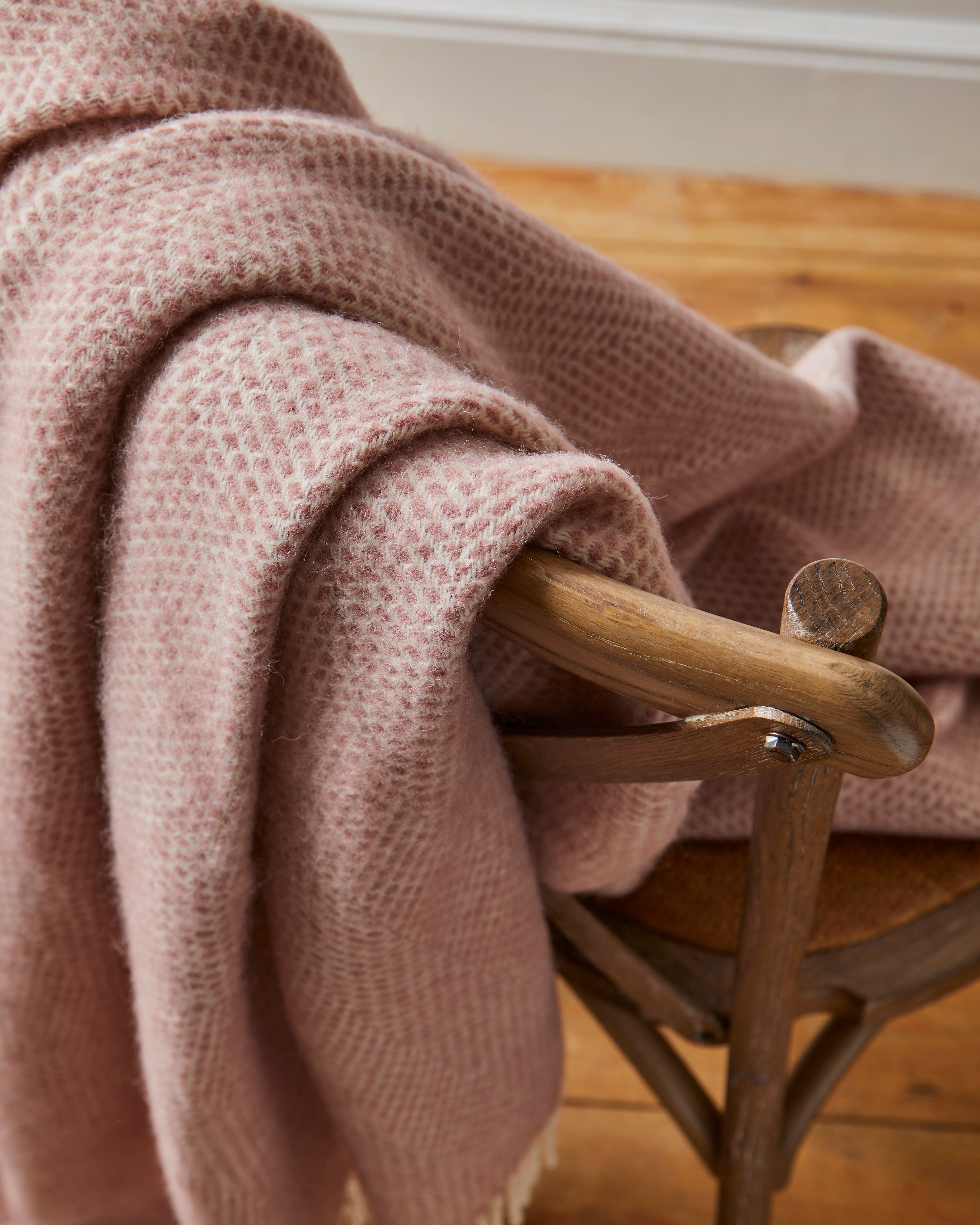 Pink textured blanket draped over a wooden chair on a wooden floor.