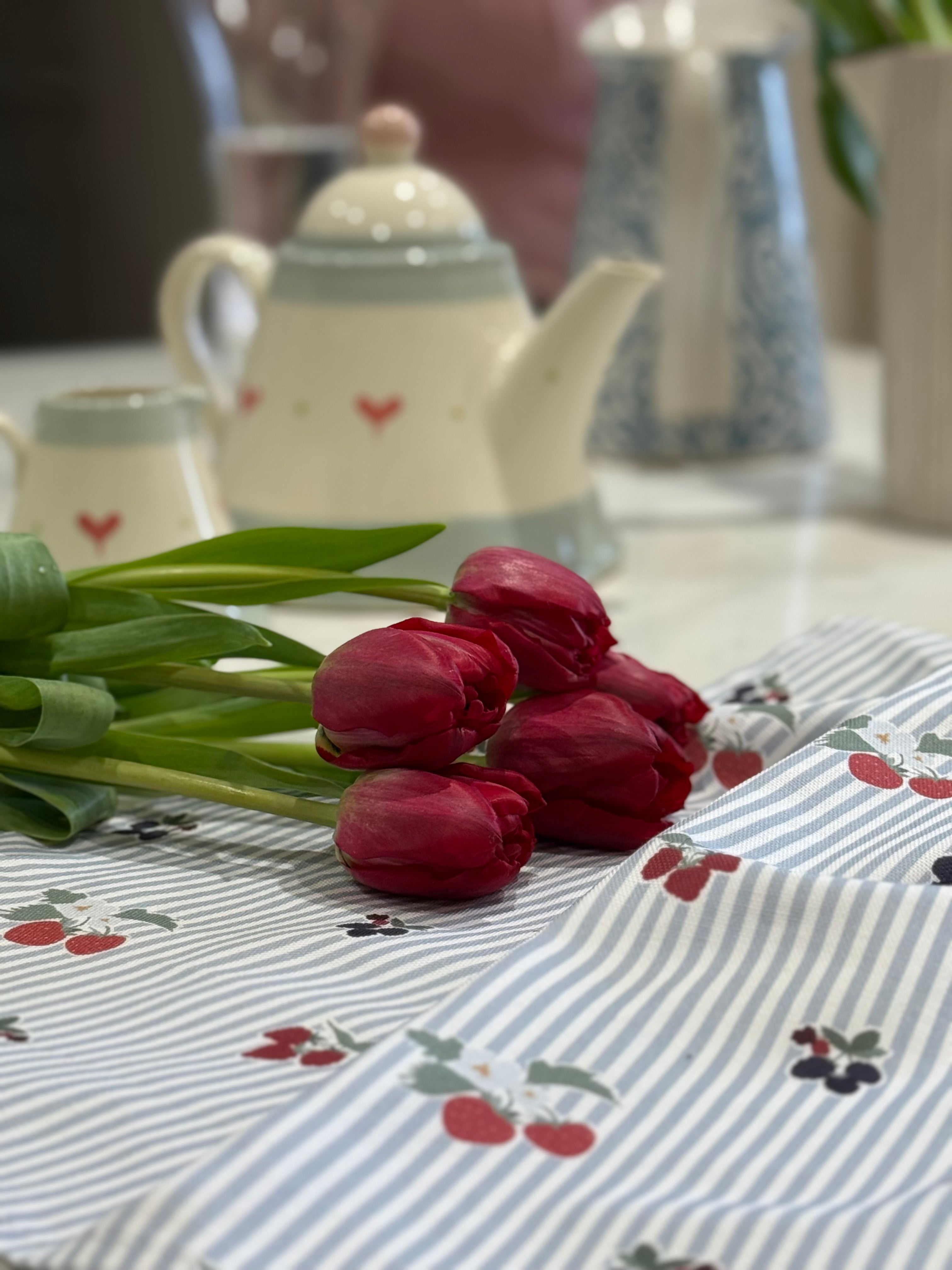Red tulips on a berry-patterned tea towel with teapots in the background