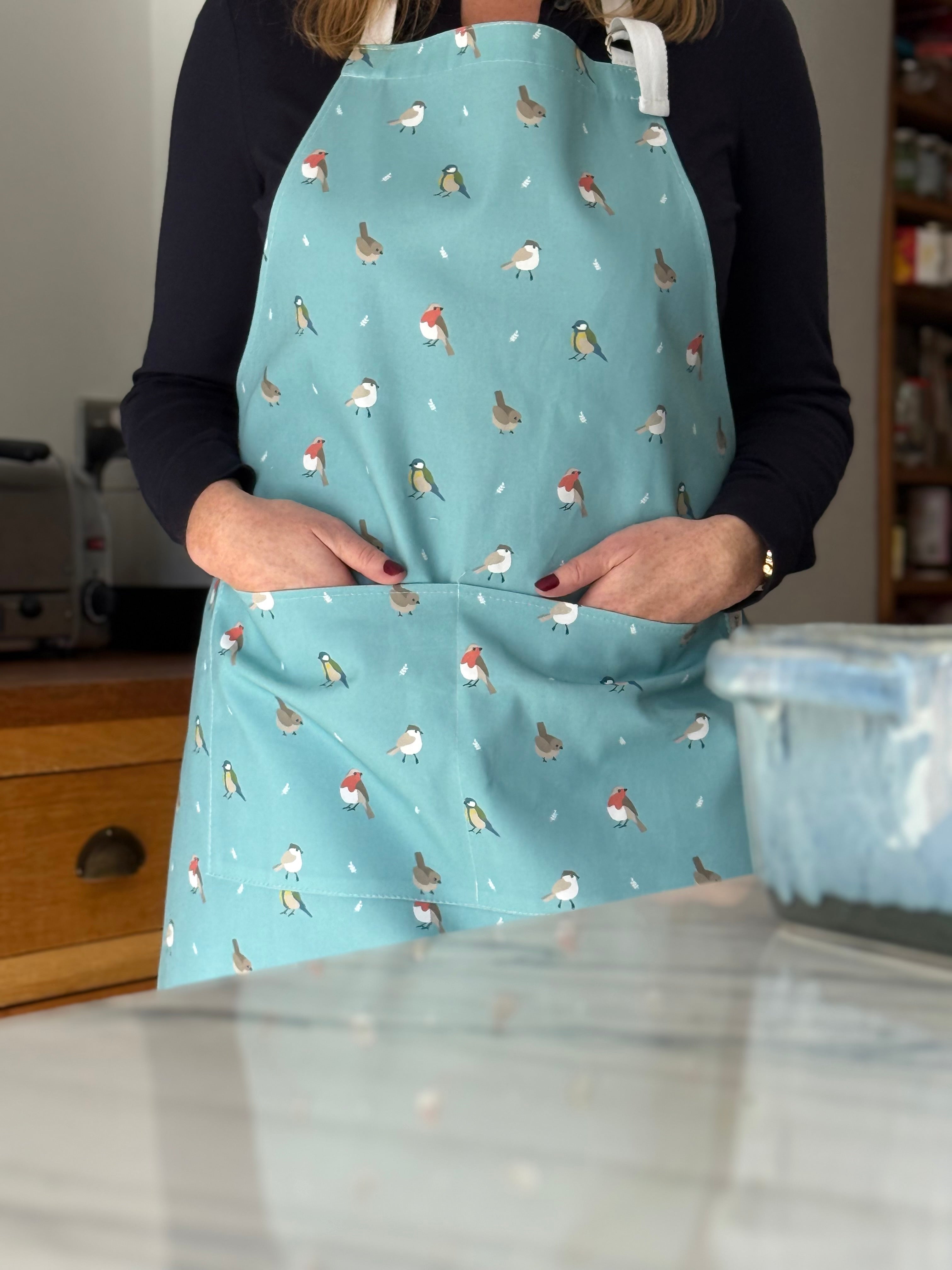 Person wearing a blue apron with bird pattern in a kitchen setting