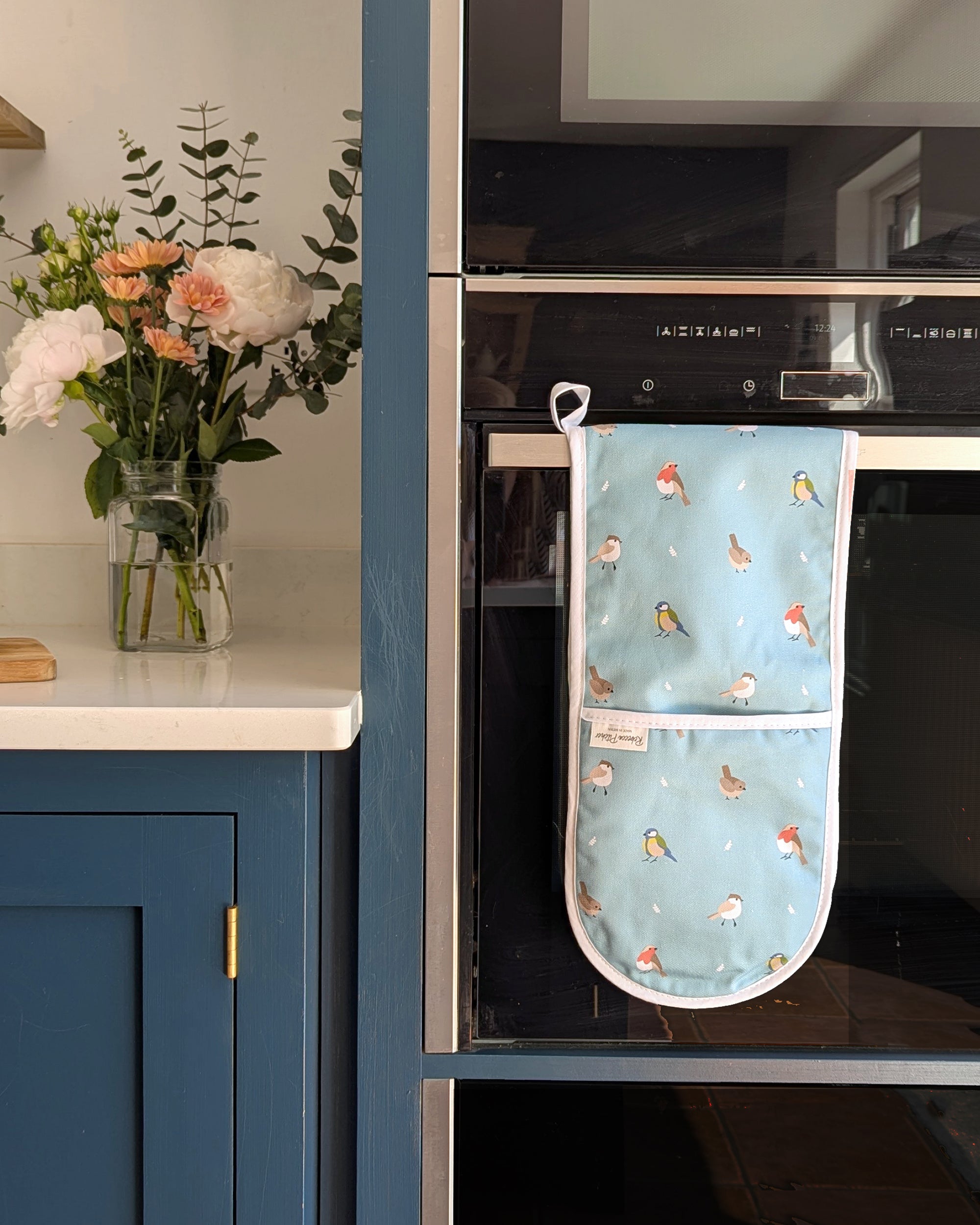 Oven mitt with bird pattern hanging on a kitchen oven.