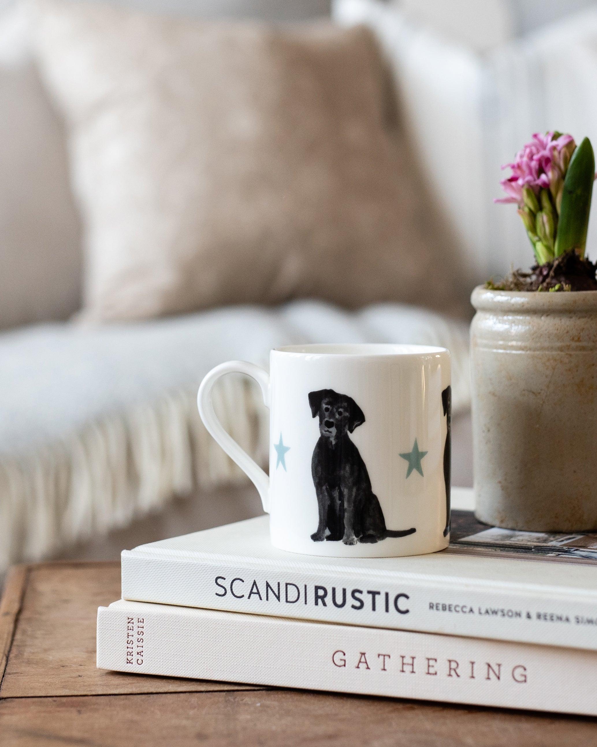 White mug with a black labrador dog illustration on a stack of books with a plant in the background