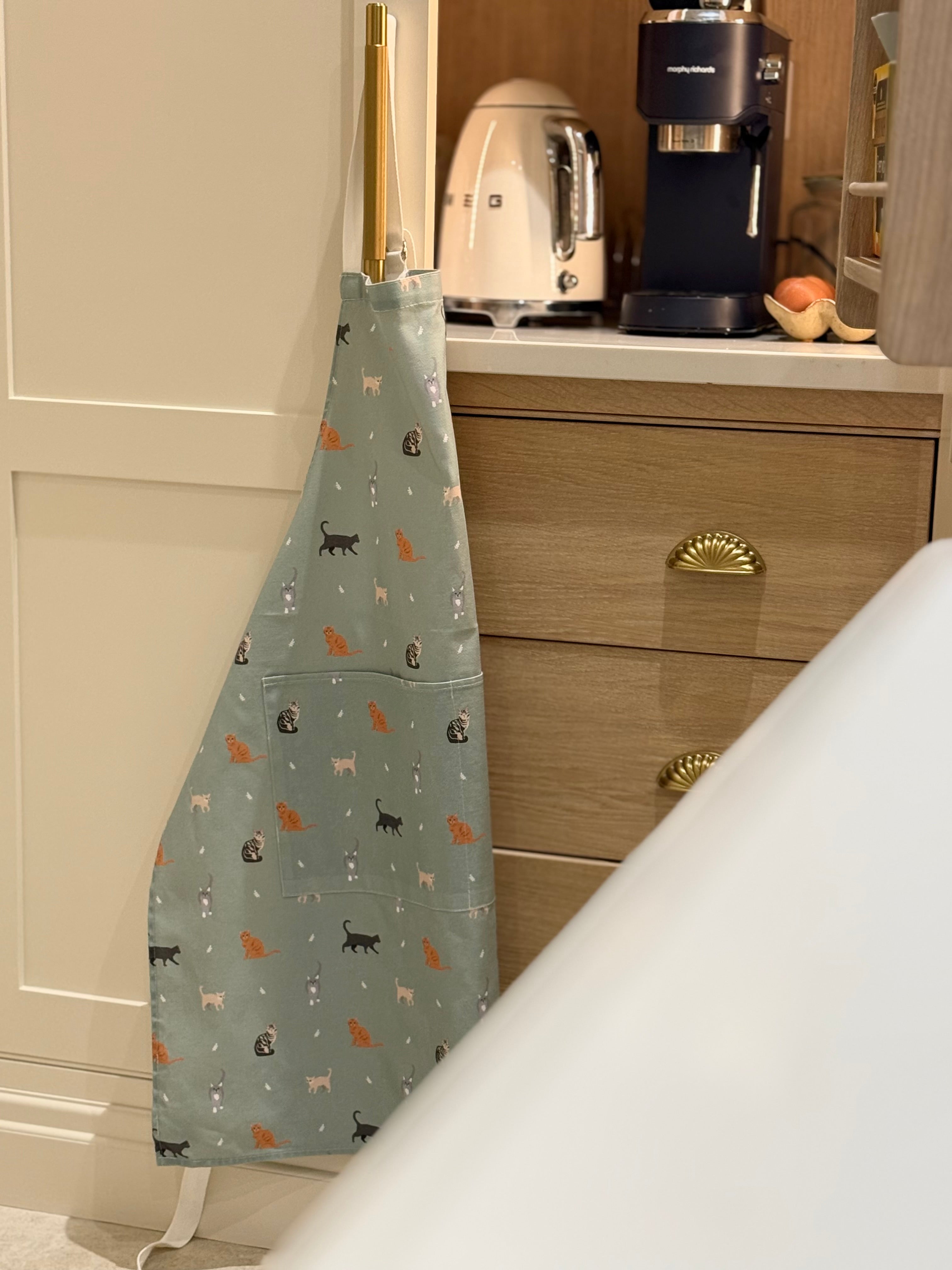Kitchen apron with cat pattern hanging on a cabinet door