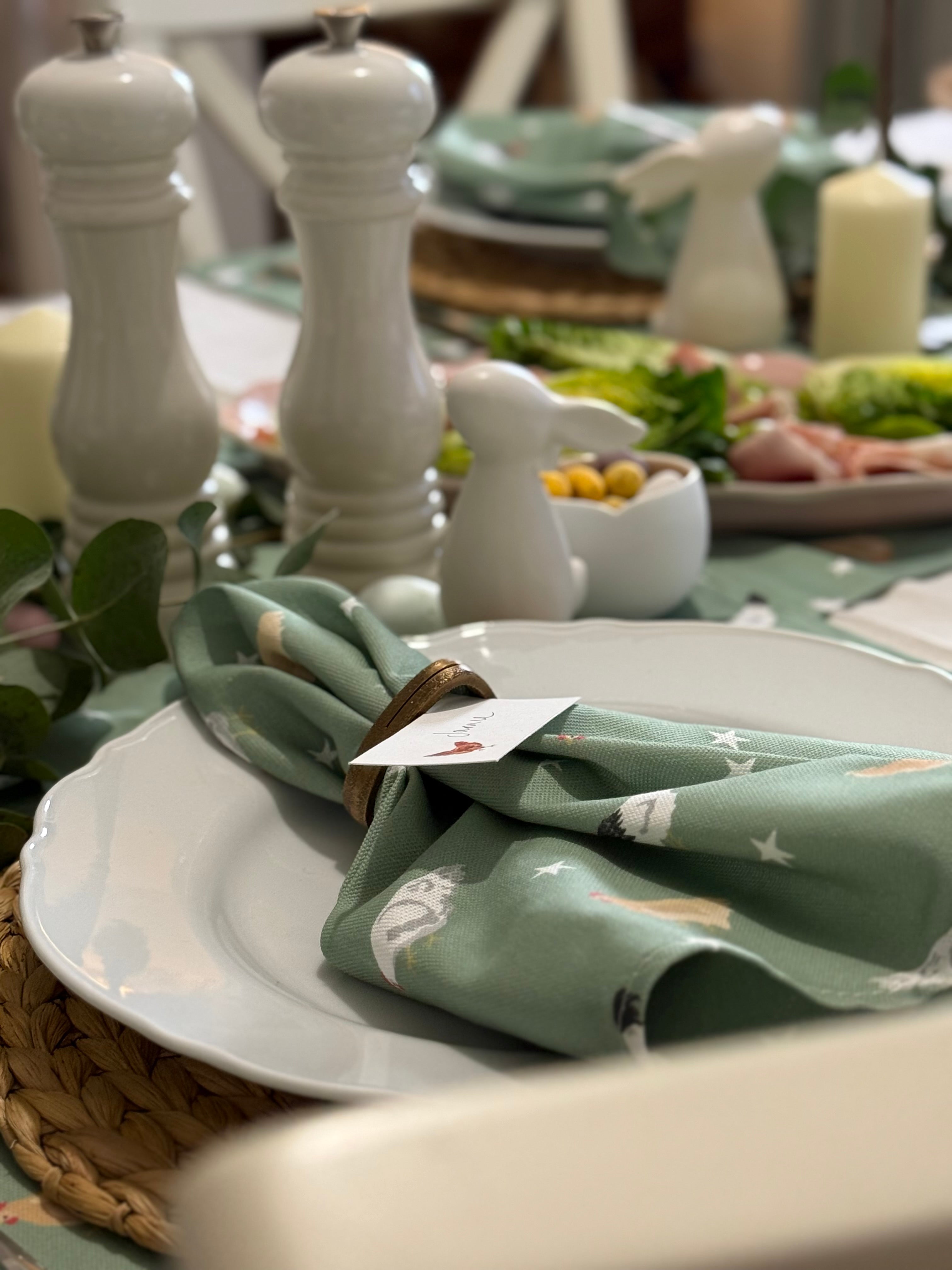 Table setting with a green chicken napkin, white salt and pepper shakers, and a card on a white plate.