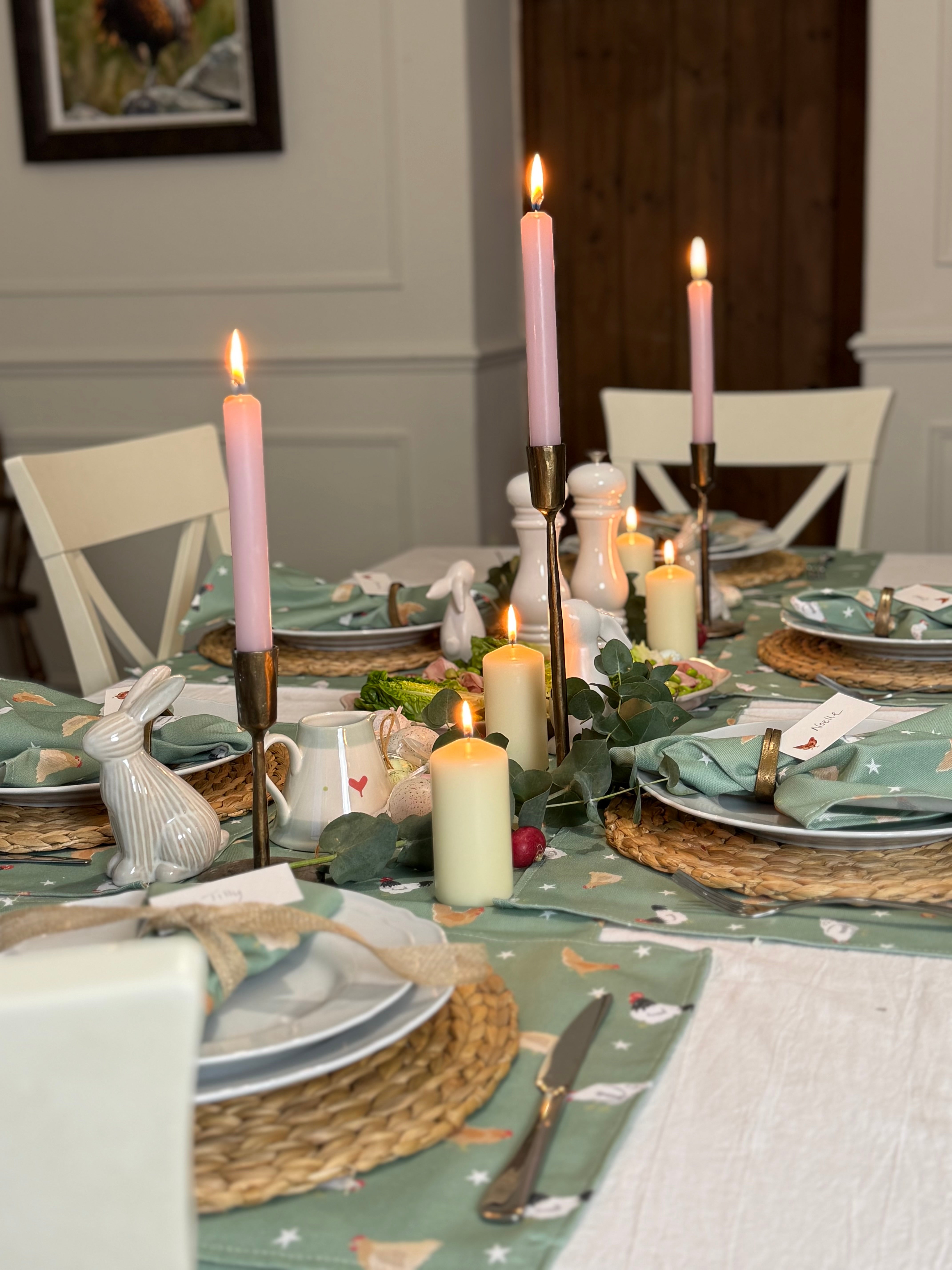 Elegant Easter table setting with chicken table linens, candles and decorative plates in a room.