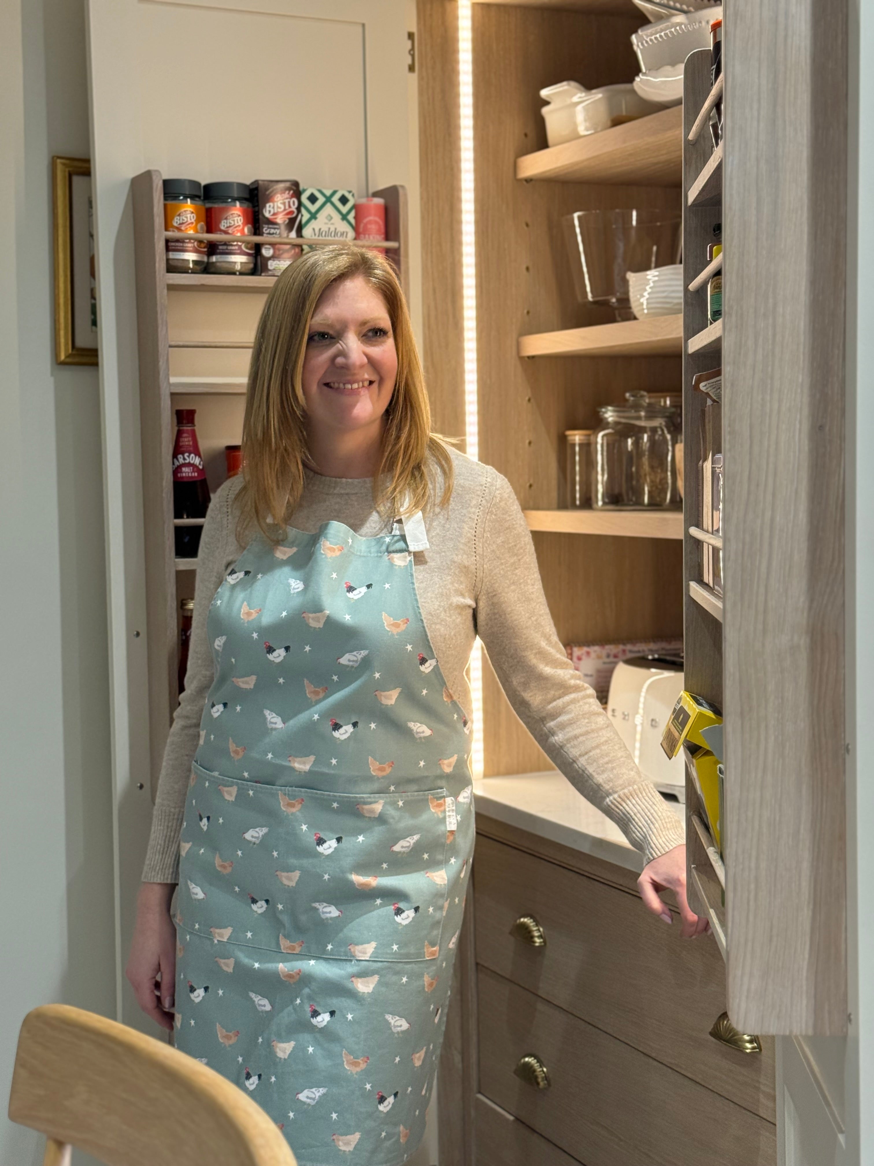 Rebecca Pitcher wearing a green chicken pattern apron in a country kitchen larder
