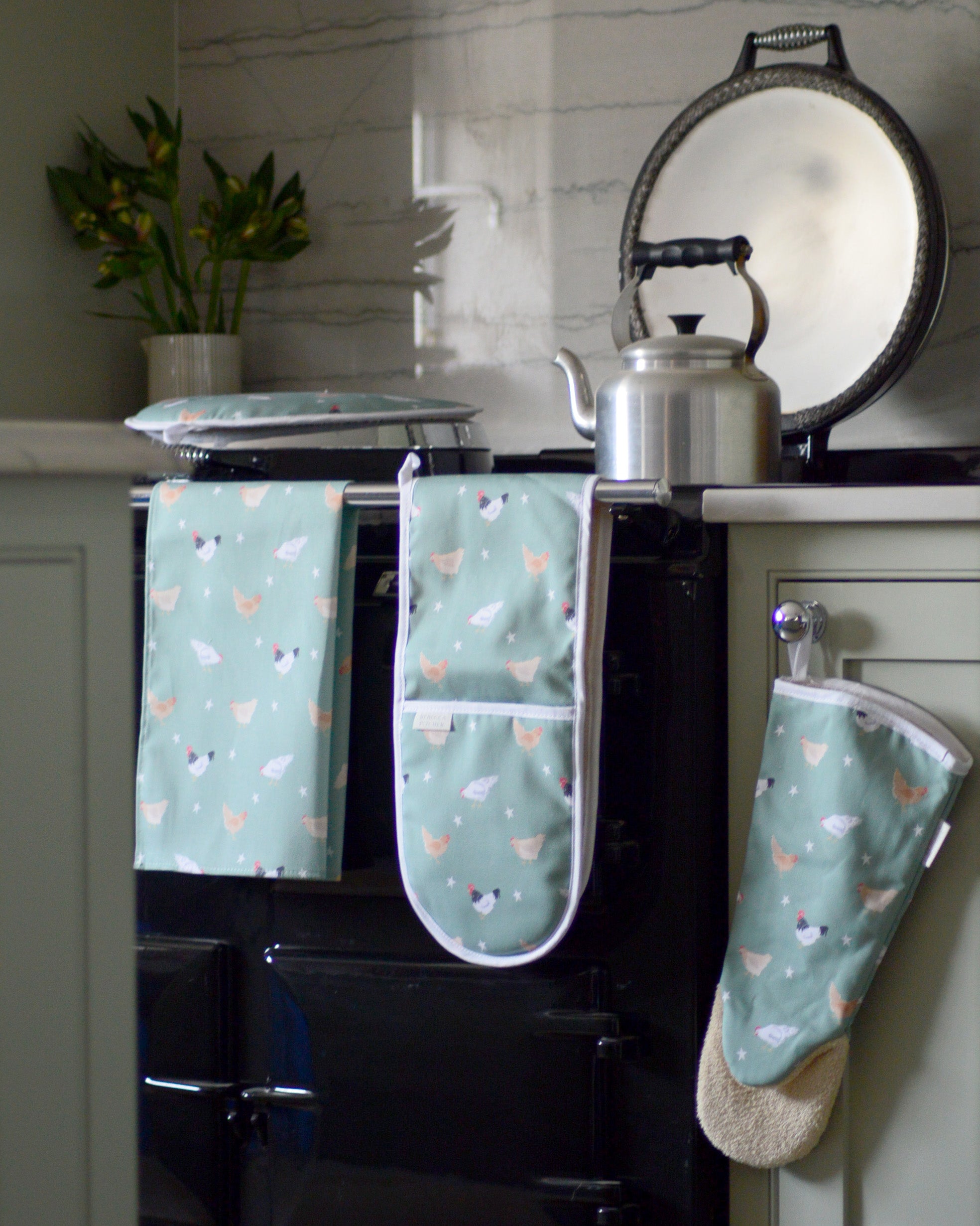Set of kitchen towels and oven mitts with chicken pattern hanging on a stove