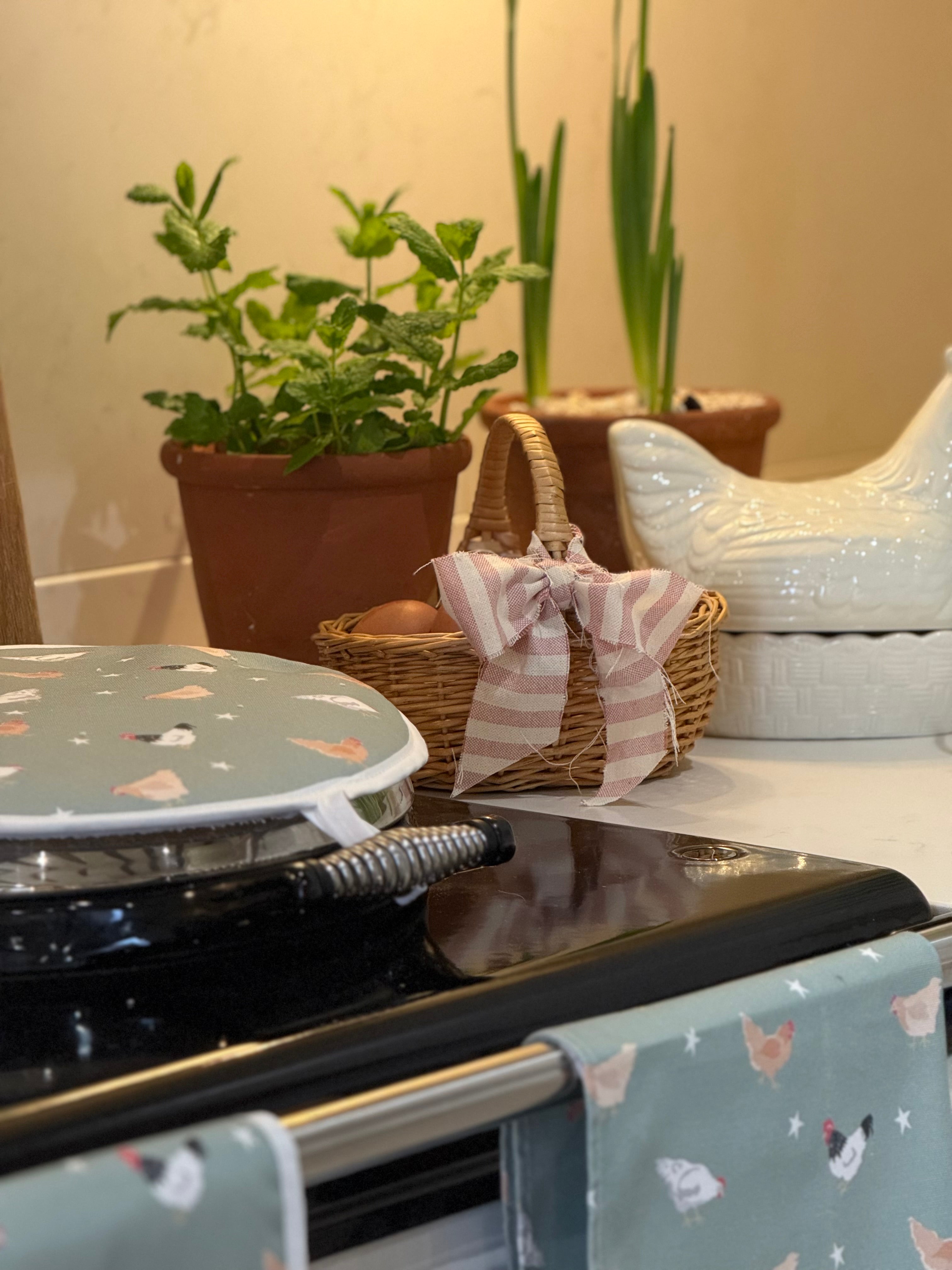 Stove with a green chicken design hob cover, potted plant, and woven basket on a countertop.