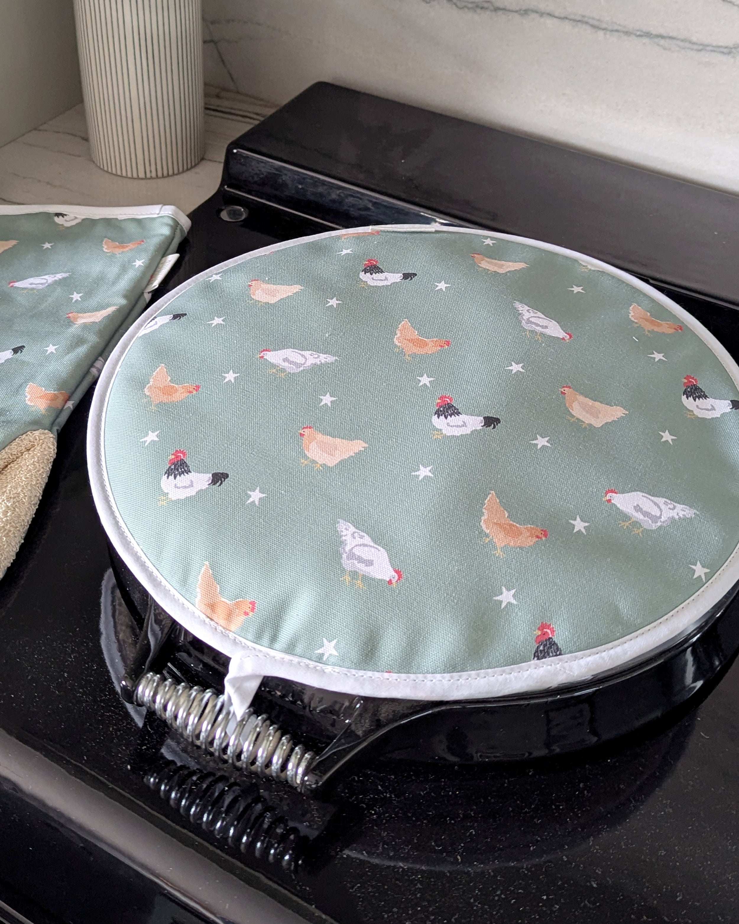 Round green hob cover with chicken pattern on a stove