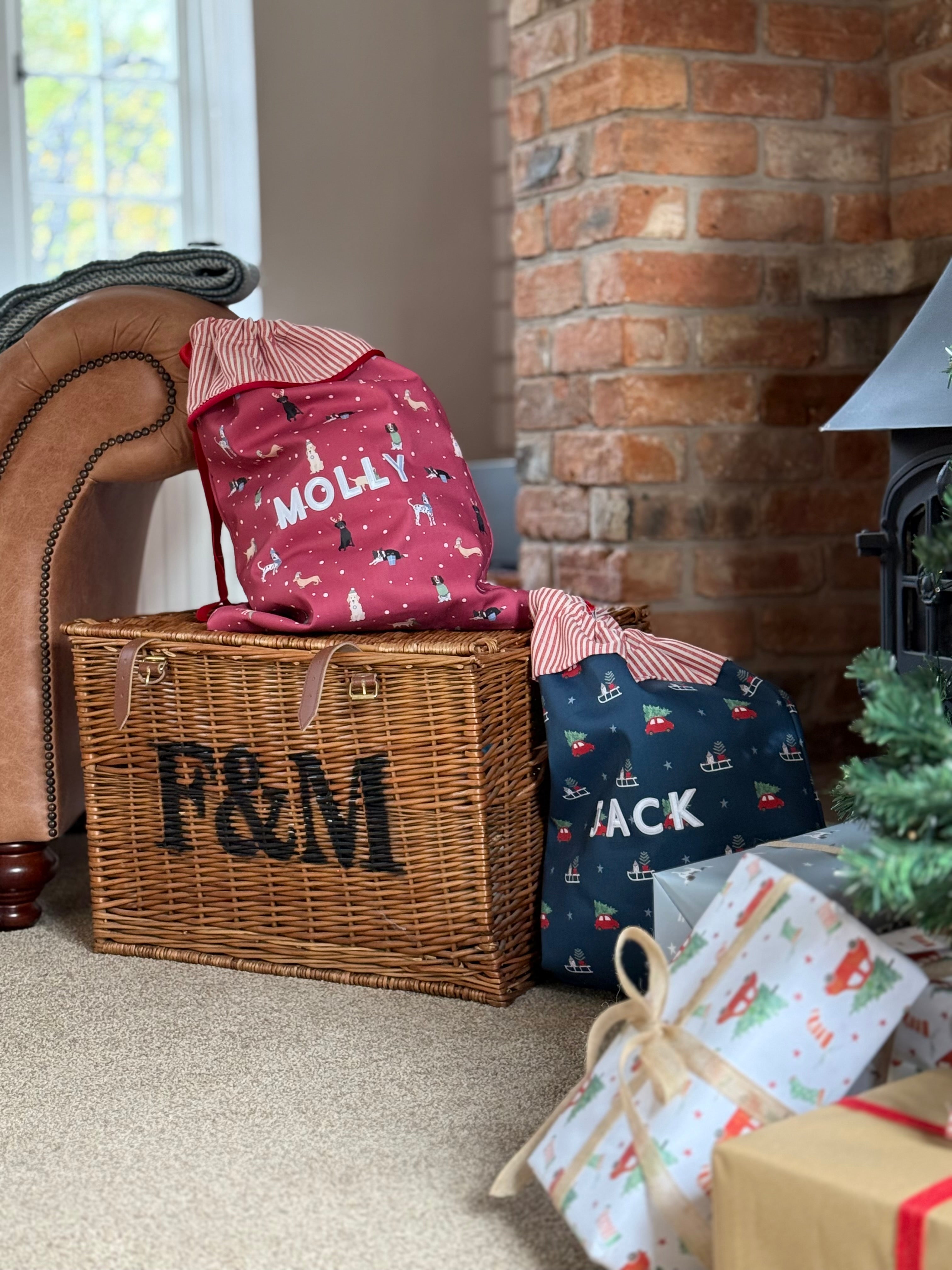 Wicker basket with personlaised Santa Sacks next to wrapped gifts in a cozy living room.