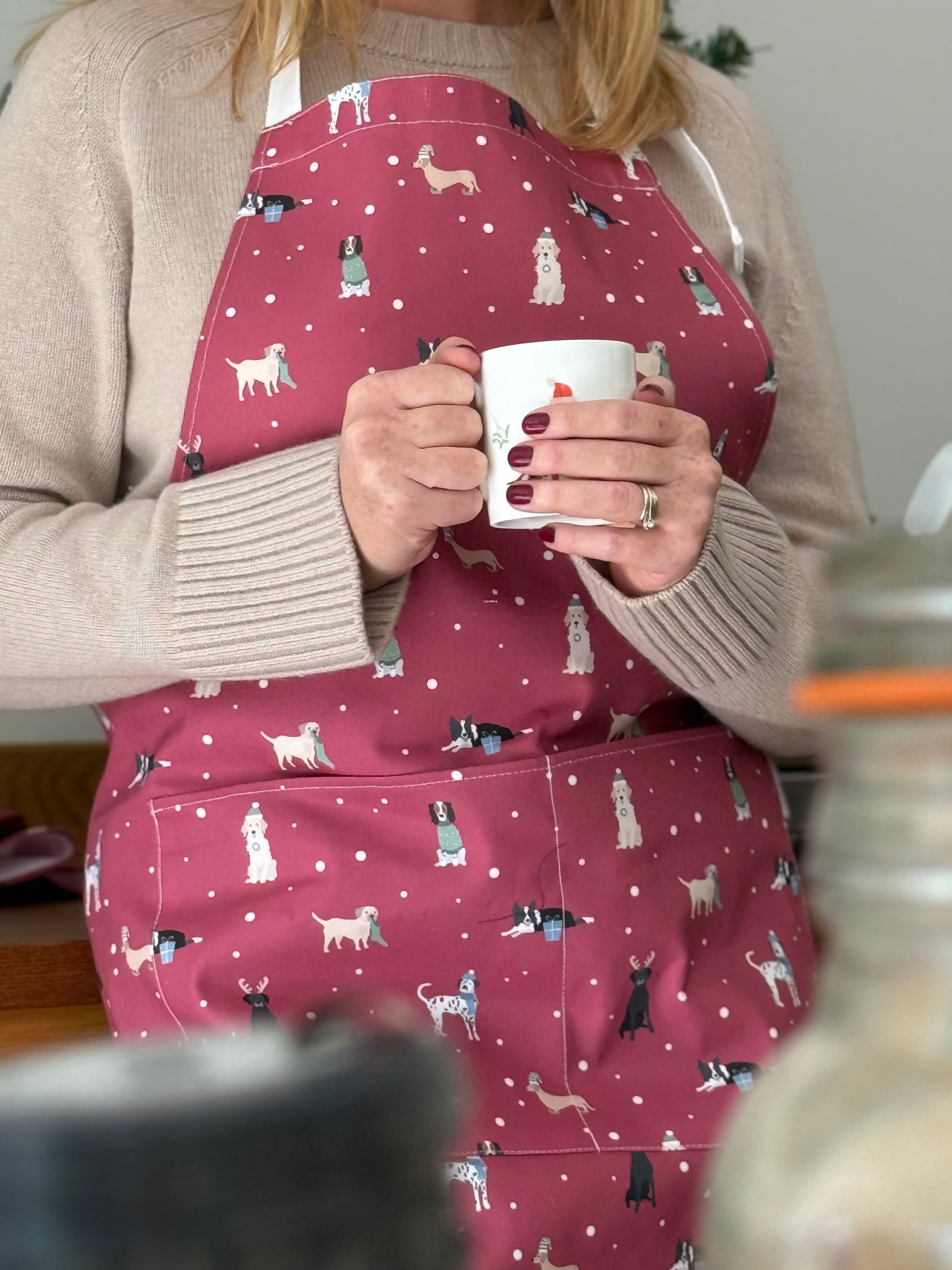 Person wearing a red apron with dog patterns, holding a white mug.
