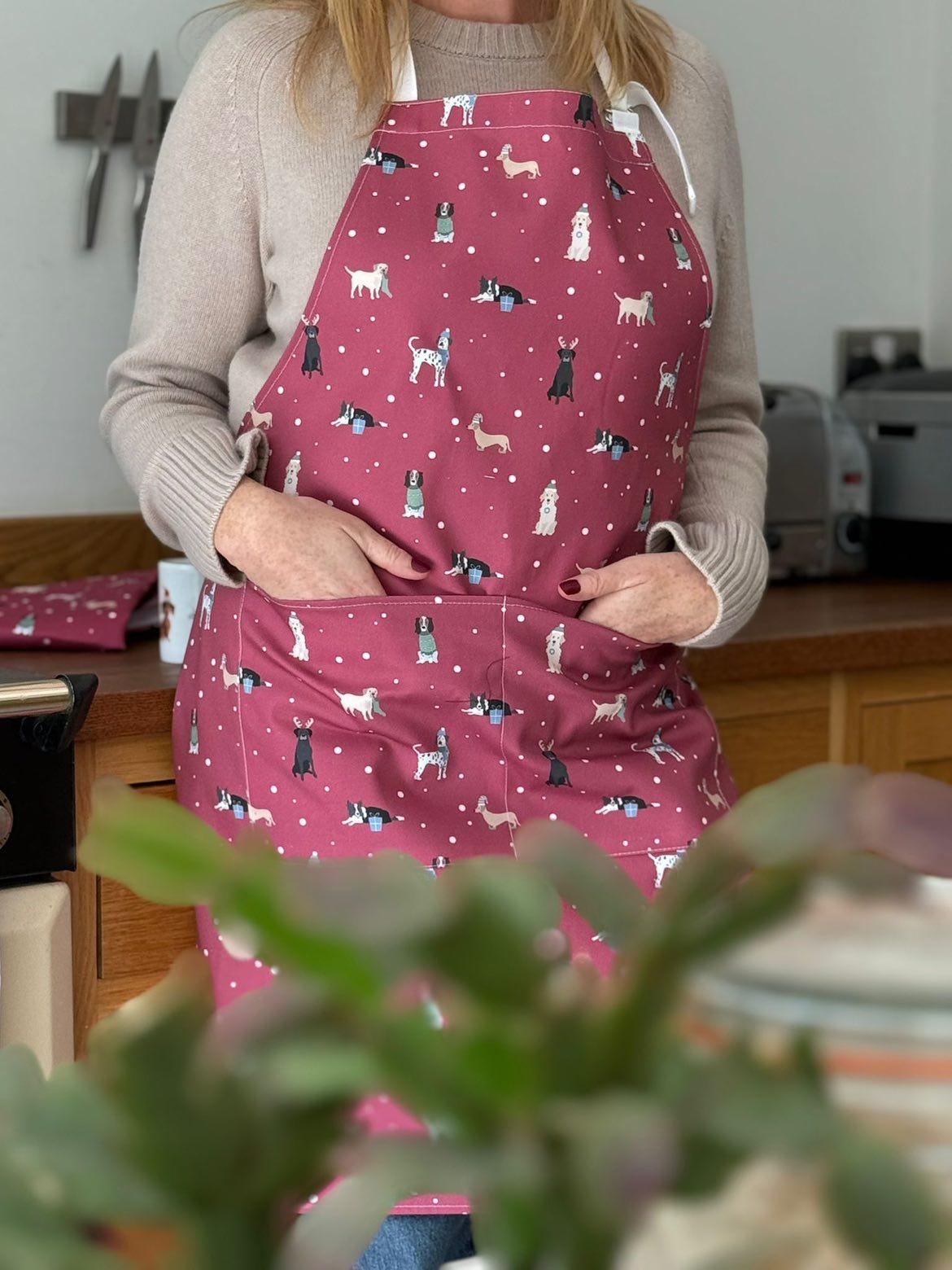 Rebecca Pitcher wearing a red Christmas apron with dog patterns in a kitchen setting