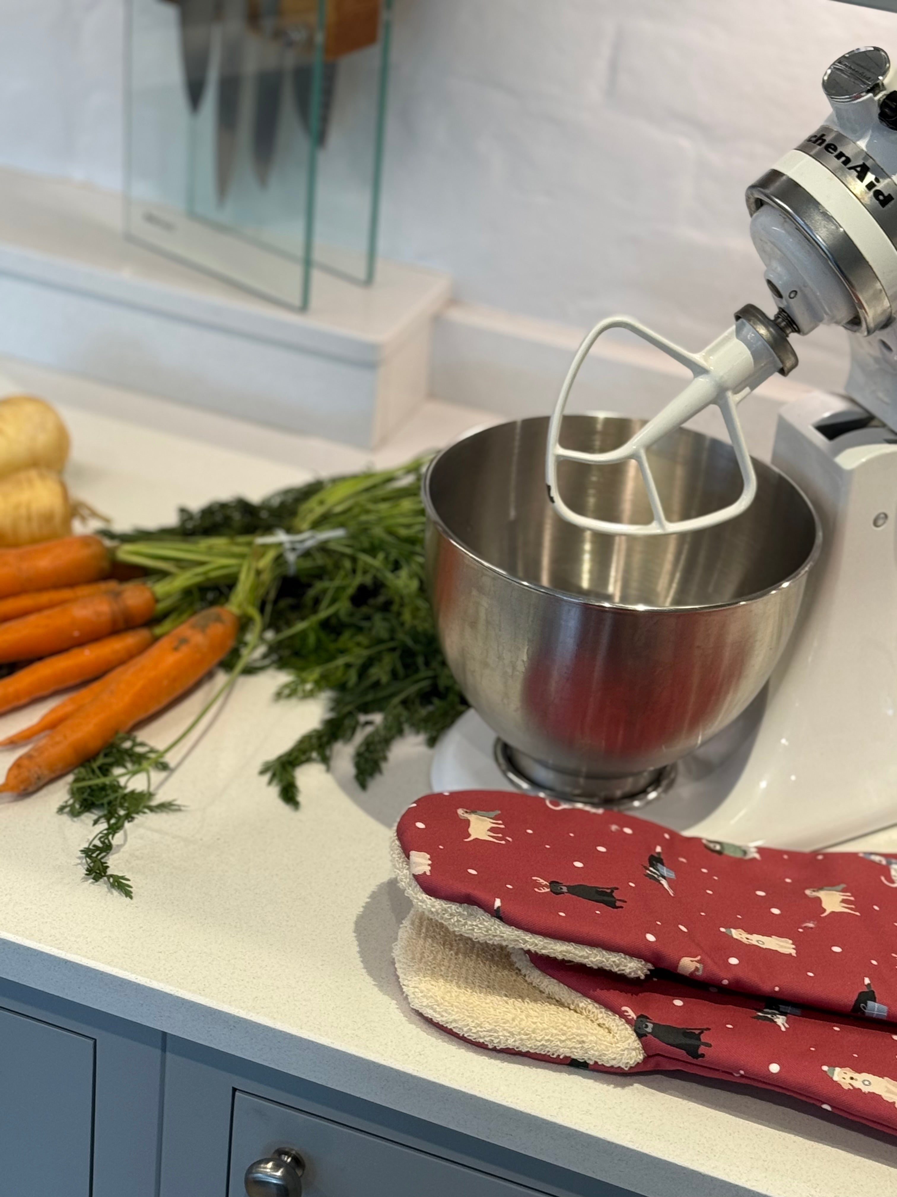 Kitchen scene with a mixer, carrots, and Christmas oven gauntlets on a countertop.