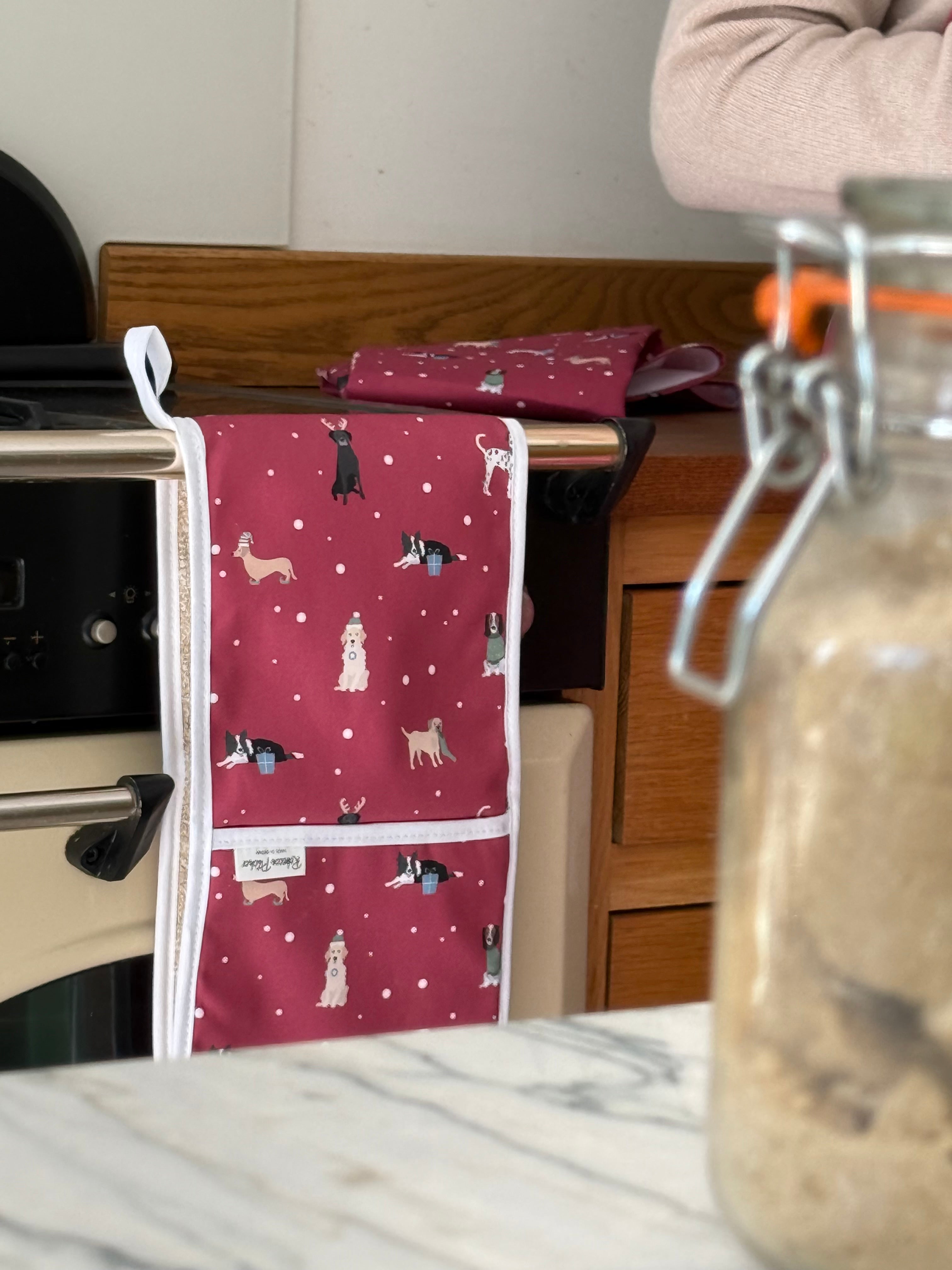 Red Christmas Dogs ovengloves and tea towel hanging on a kitchen cooker with jar of sugar in foreground