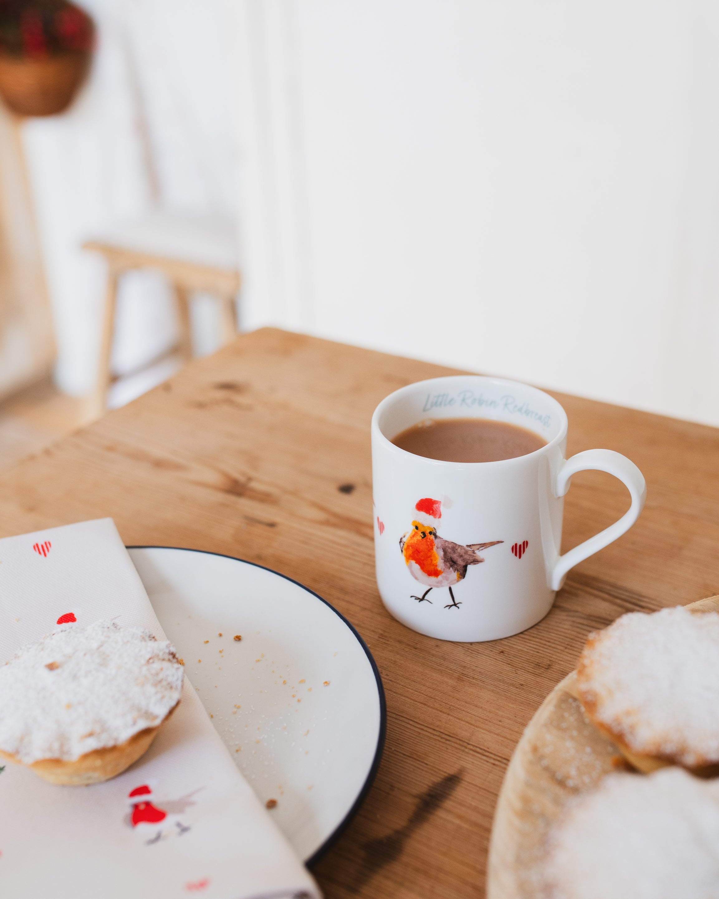White mug with a Christmas robin design on a wooden table with pastries.