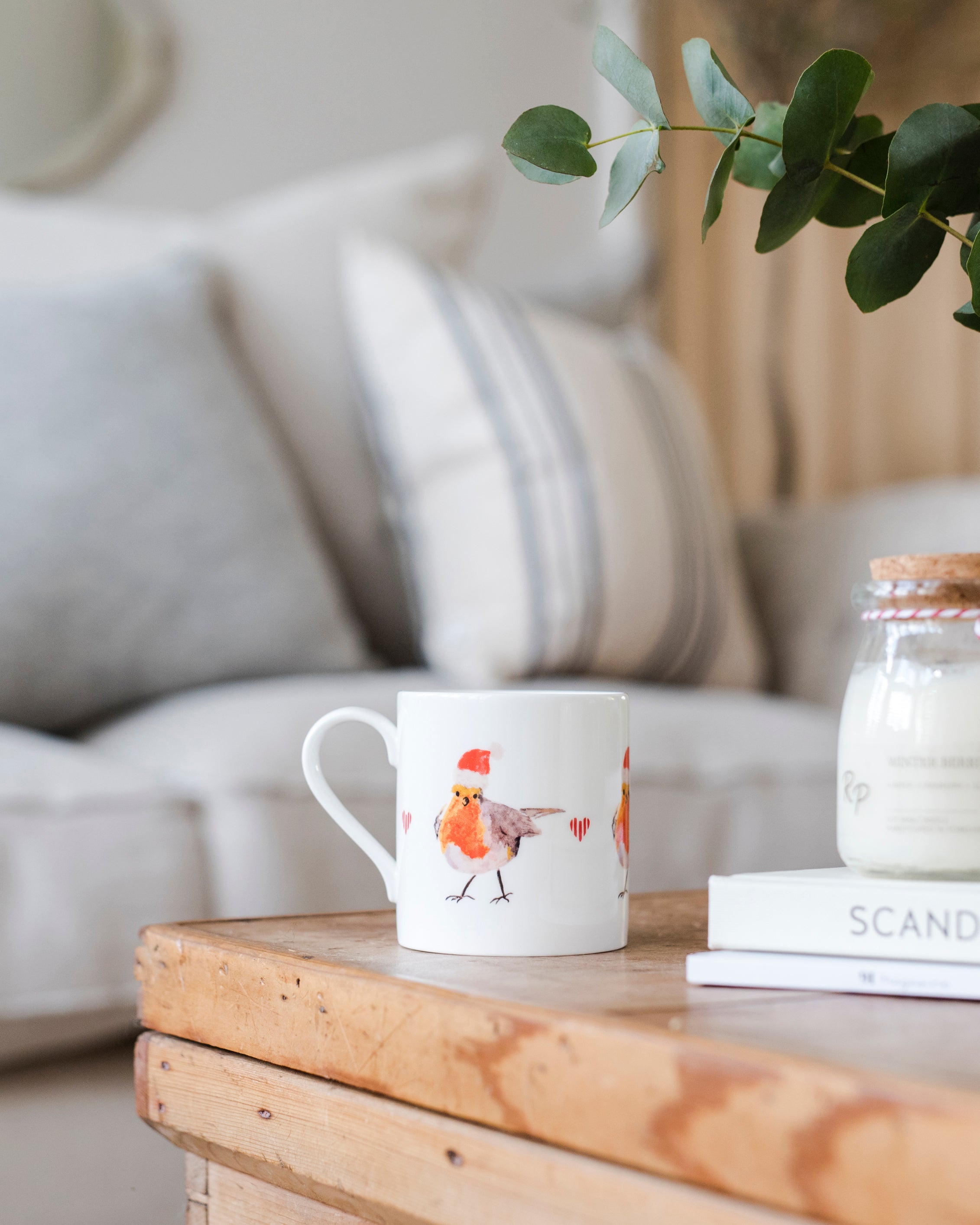 White mug with a Christmas robin design on a wooden table in a cozy living room.