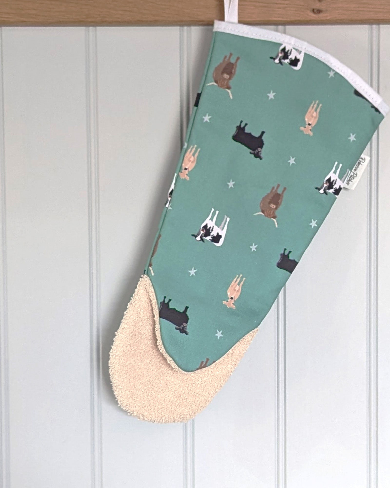 Green oven mitt with cow pattern hanging on a wooden peg rail