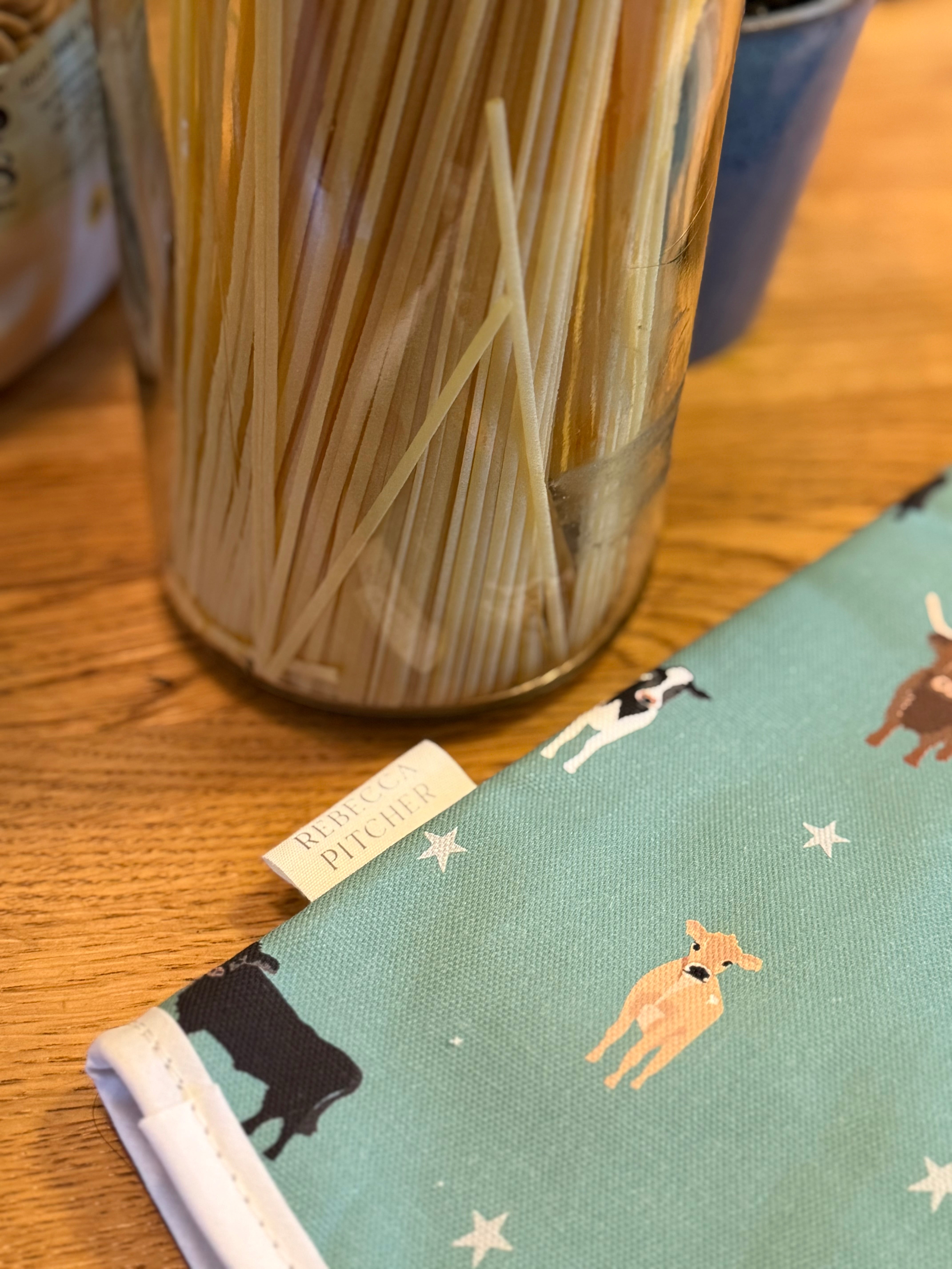 close up of green cow design oven gauntlet next to jar of pasta