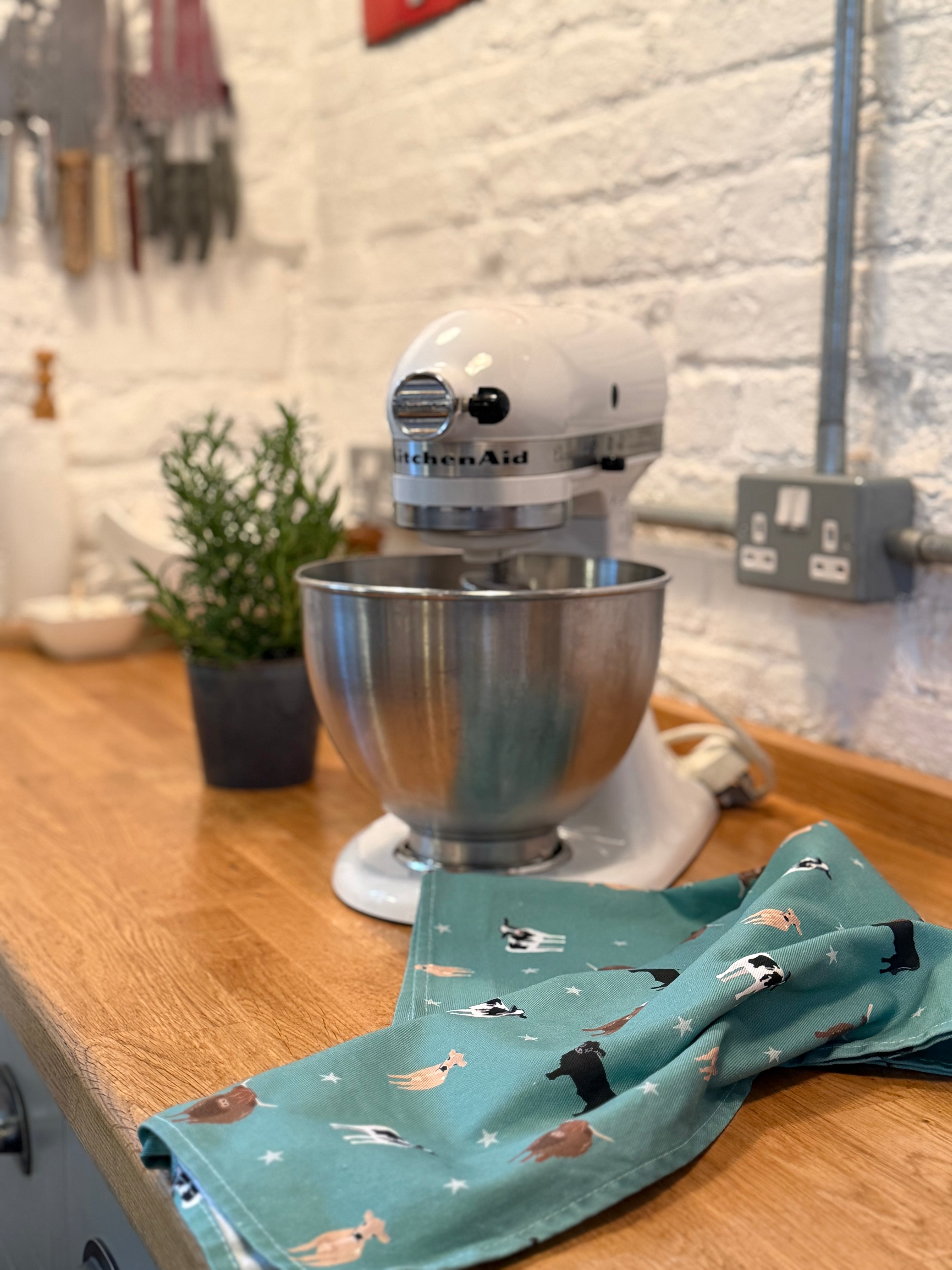 KitchenAid mixer on a wooden counter with a green cow pattern tea towel nearby