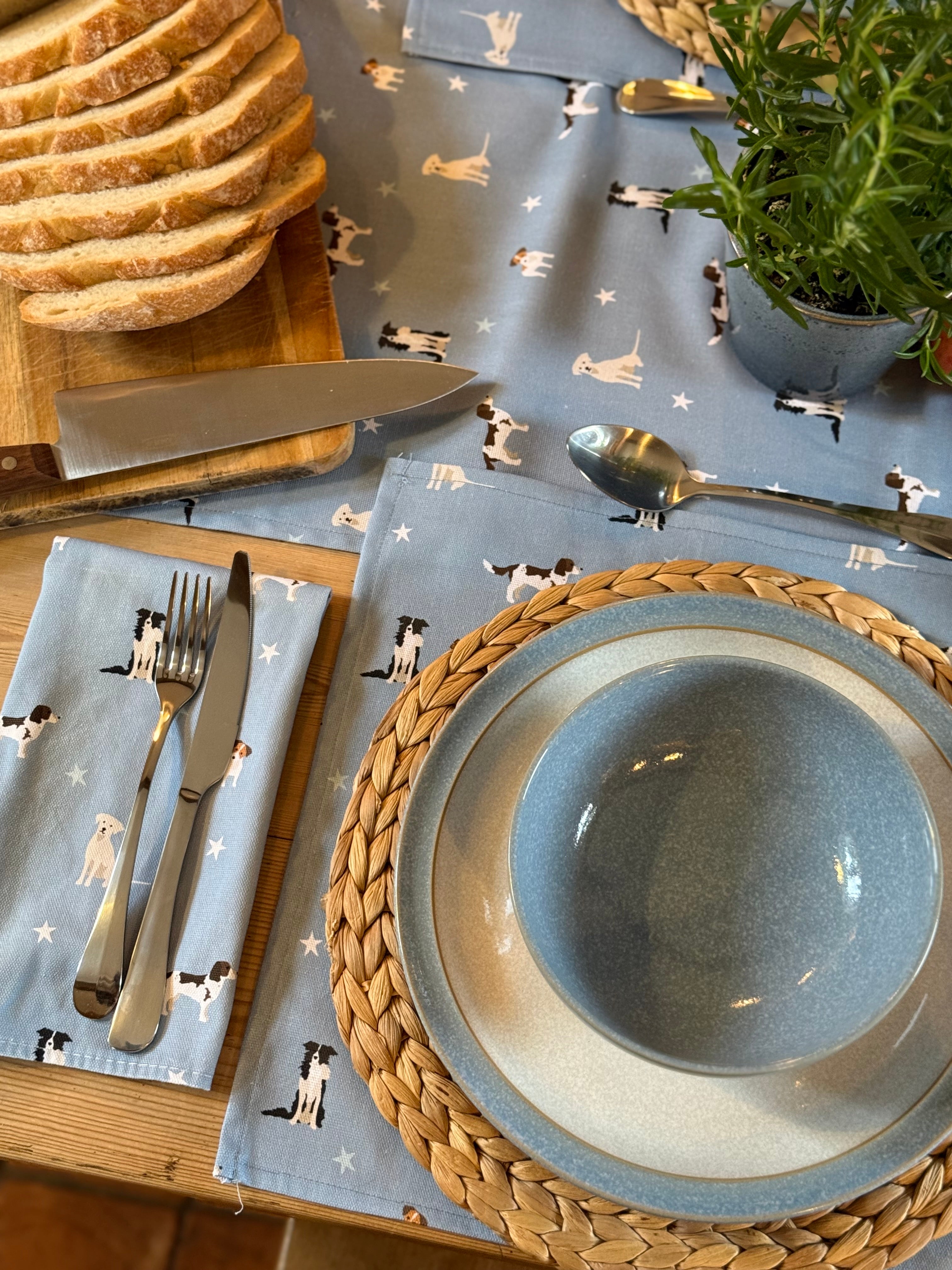 Dining table setting with blue plates, cutlery, and napkins and placemats featuring dog patterns.